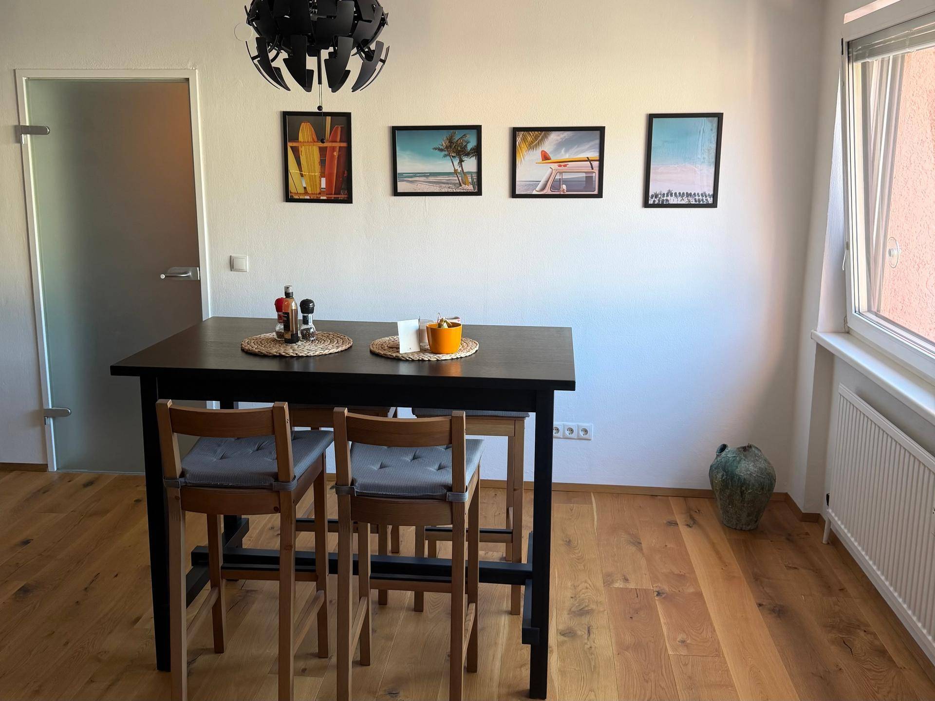 Heller Essbereich mit Holzboden, einem schwarzen Esstisch und modernen Bildern an der Wand.