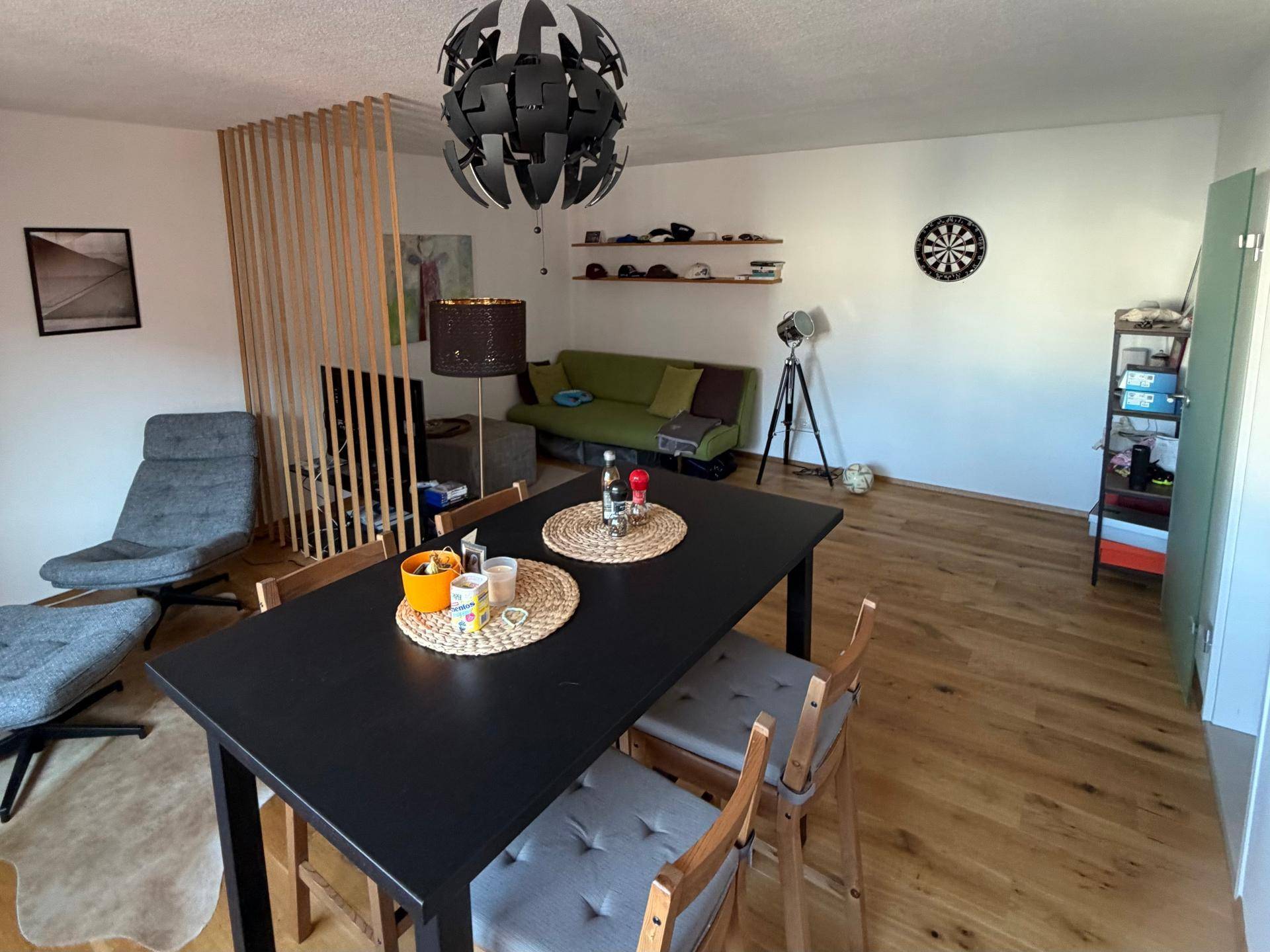 Offener Wohn- und Essbereich mit Holzboden, einem Raumteiler und gemütlichem Sofa.