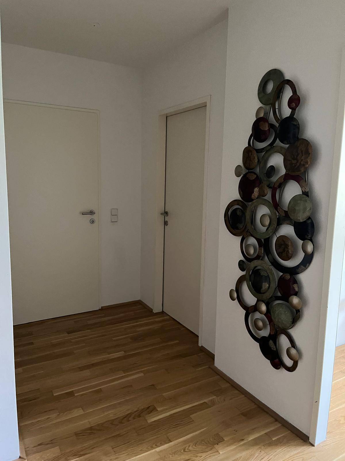 Heller Flur mit Holzboden und dekorativer Wandkunst, der zu weiteren Räumen führt.