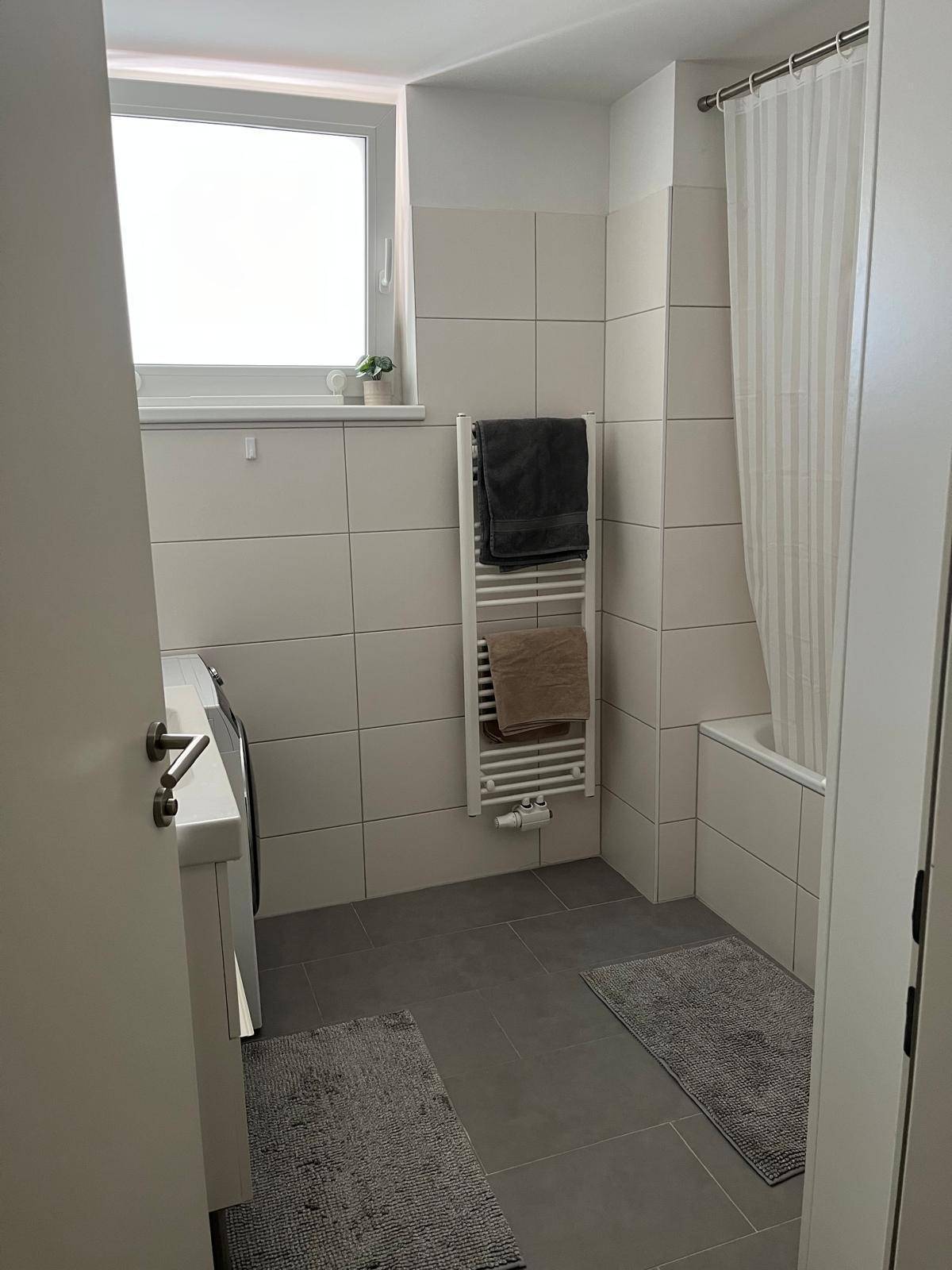 Modernes Badezimmer mit Badewanne, Duschvorhang, Handtuchheizkörper und Fliesenboden.