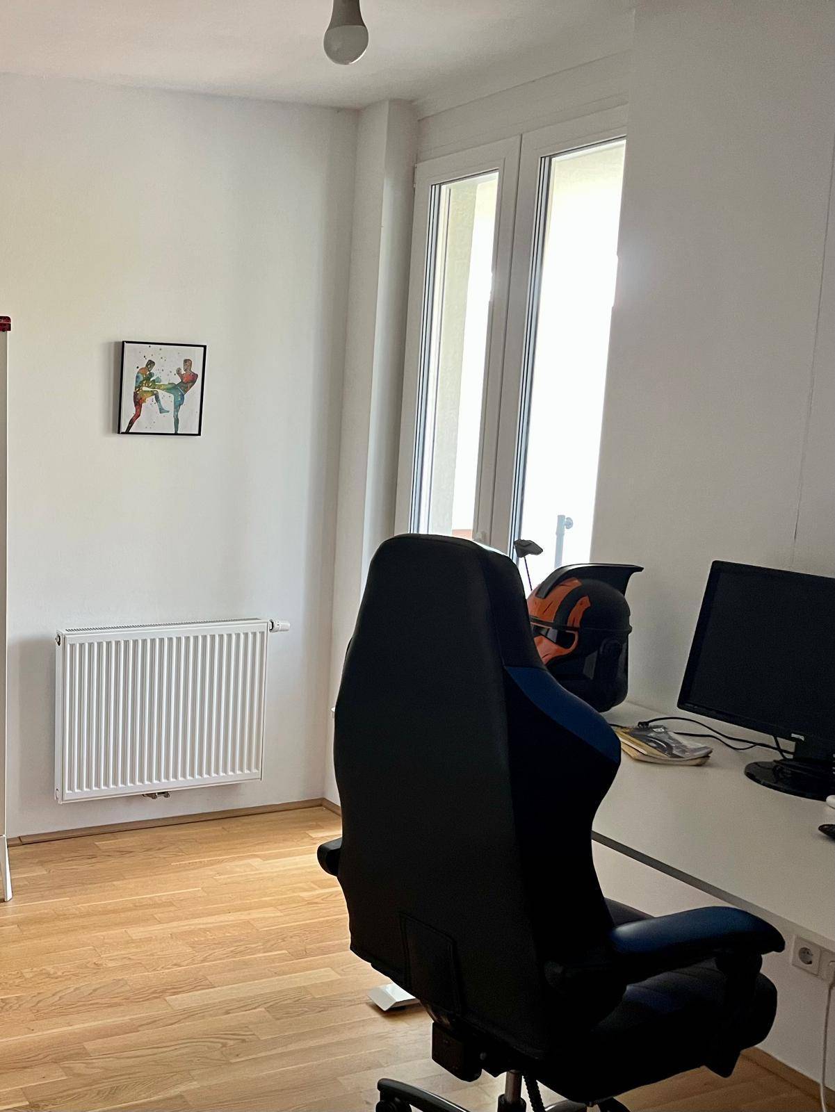 Helles Zimmer mit Schreibtisch, Gaming-Stuhl und großem Fenster, das viel Licht hereinlässt.
