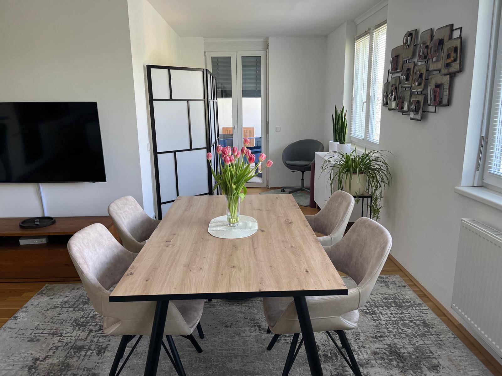 Essbereich mit Holztisch, beigen Stühlen und Zugang zu einem Balkon oder einer Terrasse.