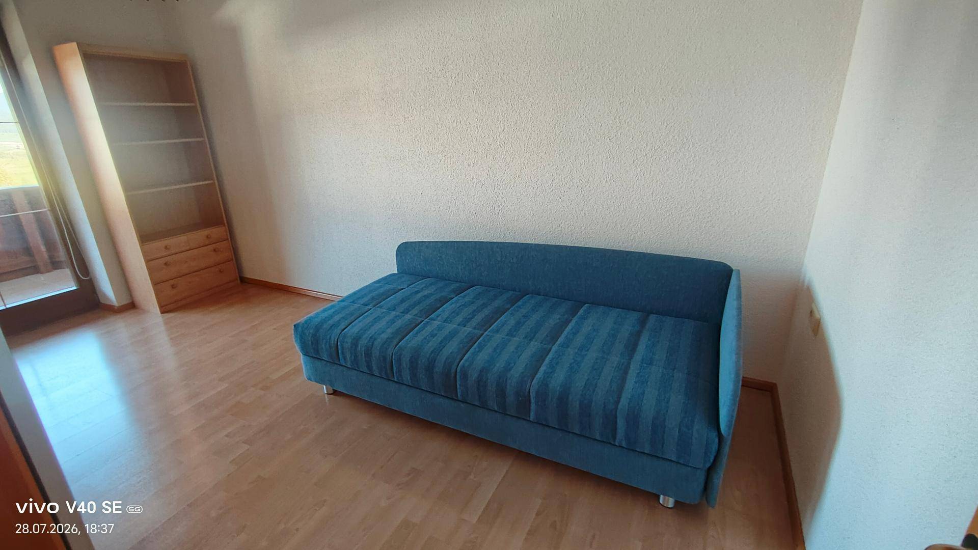 Helles Gästezimmer mit blauem Schlafsofa und Bücherregal, ideal für Besucher.