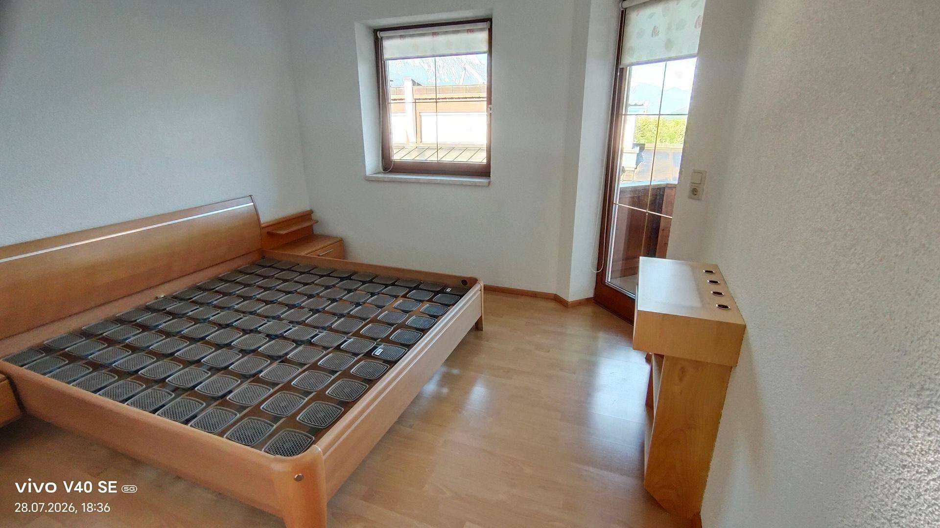 Schlafzimmer mit Holzbett und Zugang zu einem Balkon oder einer Terrasse, hell und freundlich.