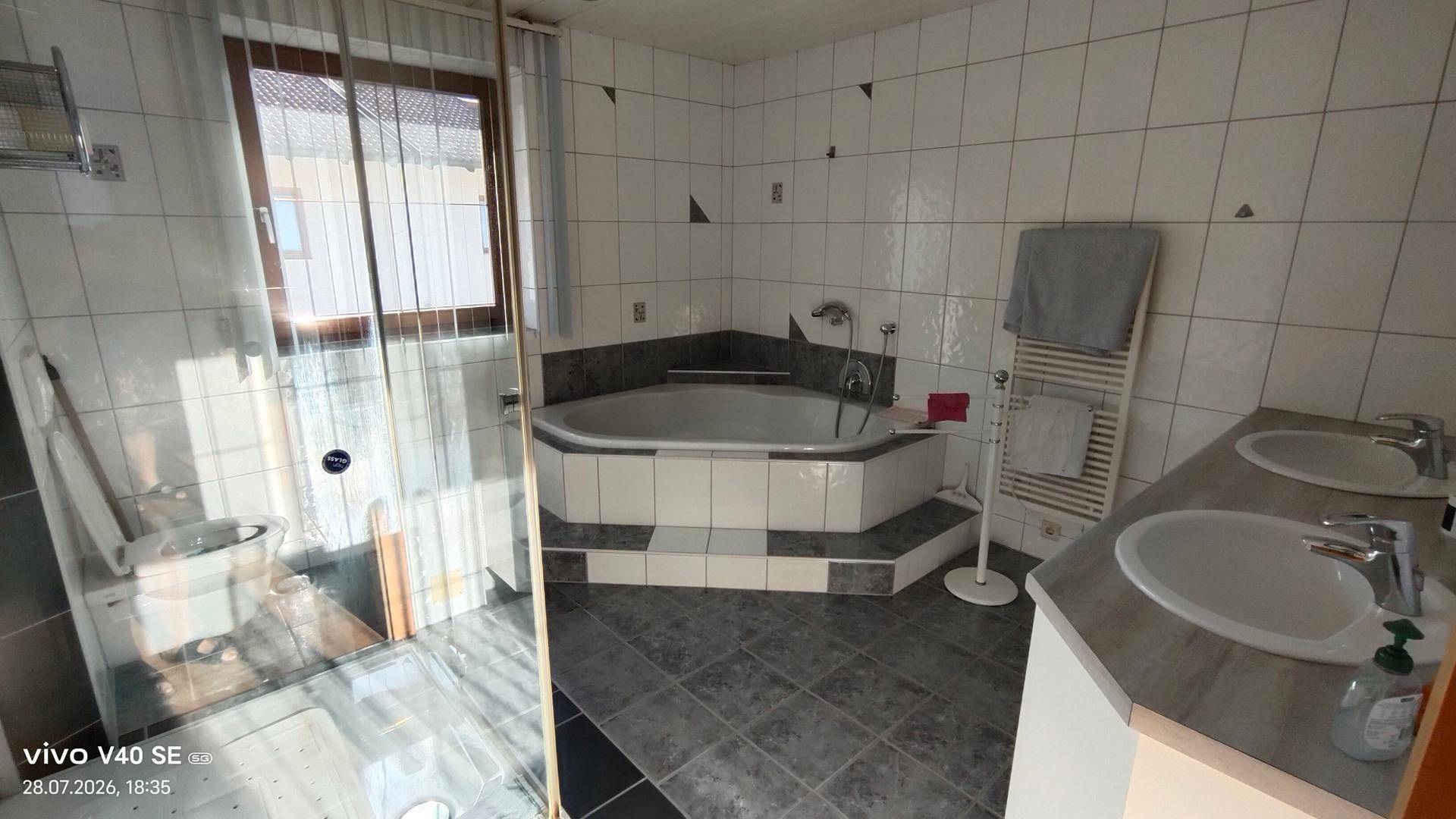 Geräumiges Badezimmer mit Eckbadewanne, Dusche, Doppelwaschbecken und Fenster.