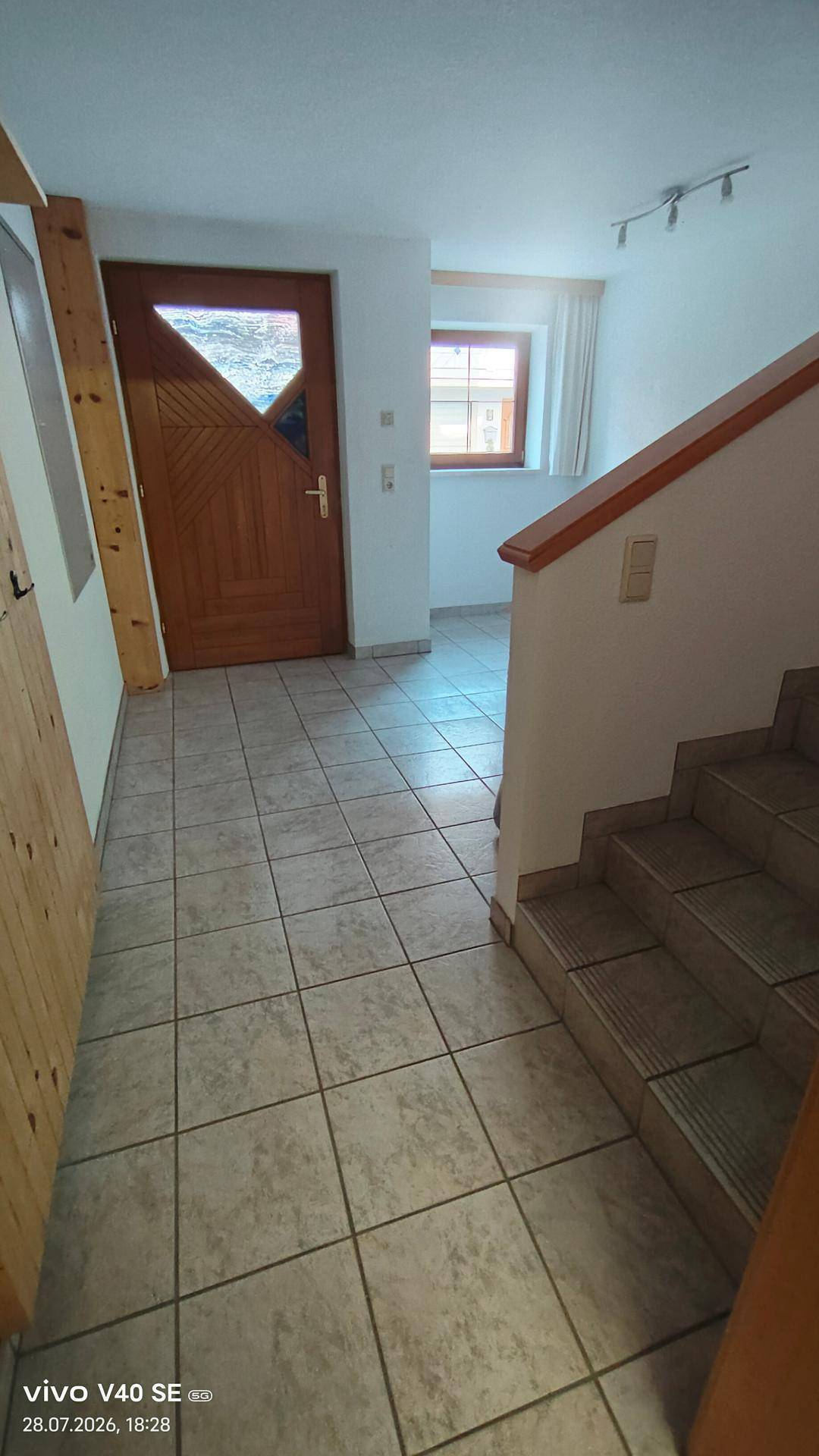 Heller Eingangsbereich mit Fliesenboden, Holztreppe und einer einladenden Haustür.
