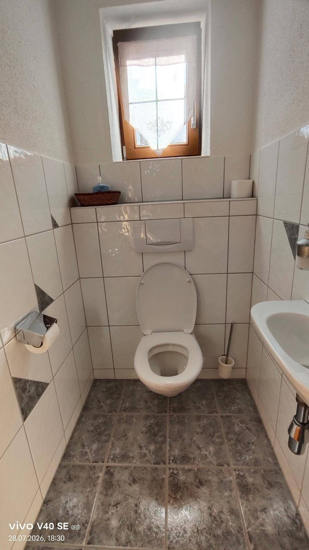 Kleines Gäste-WC mit Fenster, Wand-WC und Fliesenboden in neutralen Farben.