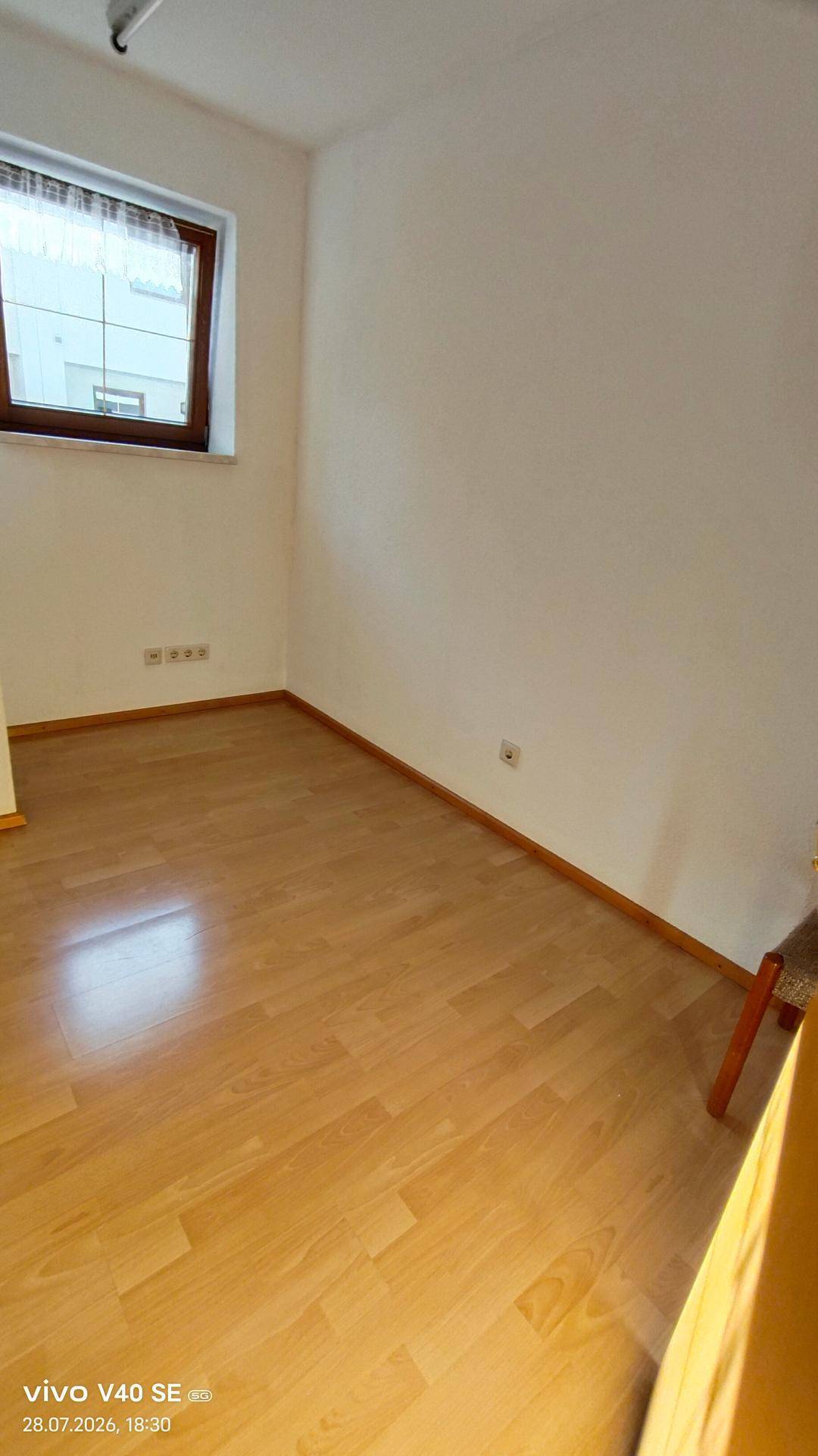 Leeres Zimmer mit hellem Holzboden und einem Fenster, bereit zur individuellen Gestaltung.