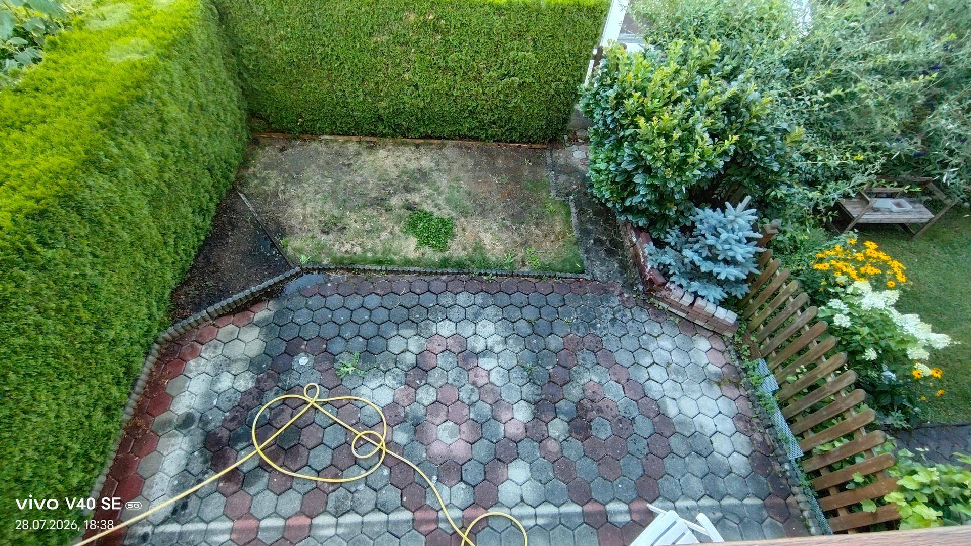 Gepflasterte Terrasse mit Hecken und Grünflächen, ideal für entspannte Stunden im Freien.