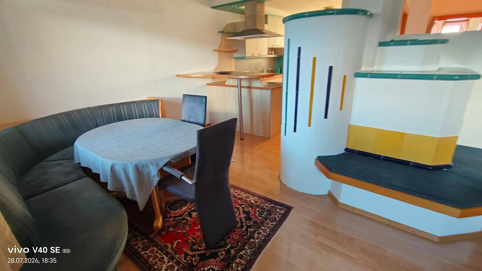 Gemütlicher Essbereich mit rundem Tisch und traditionellem Kachelofen, offen zur Küche.