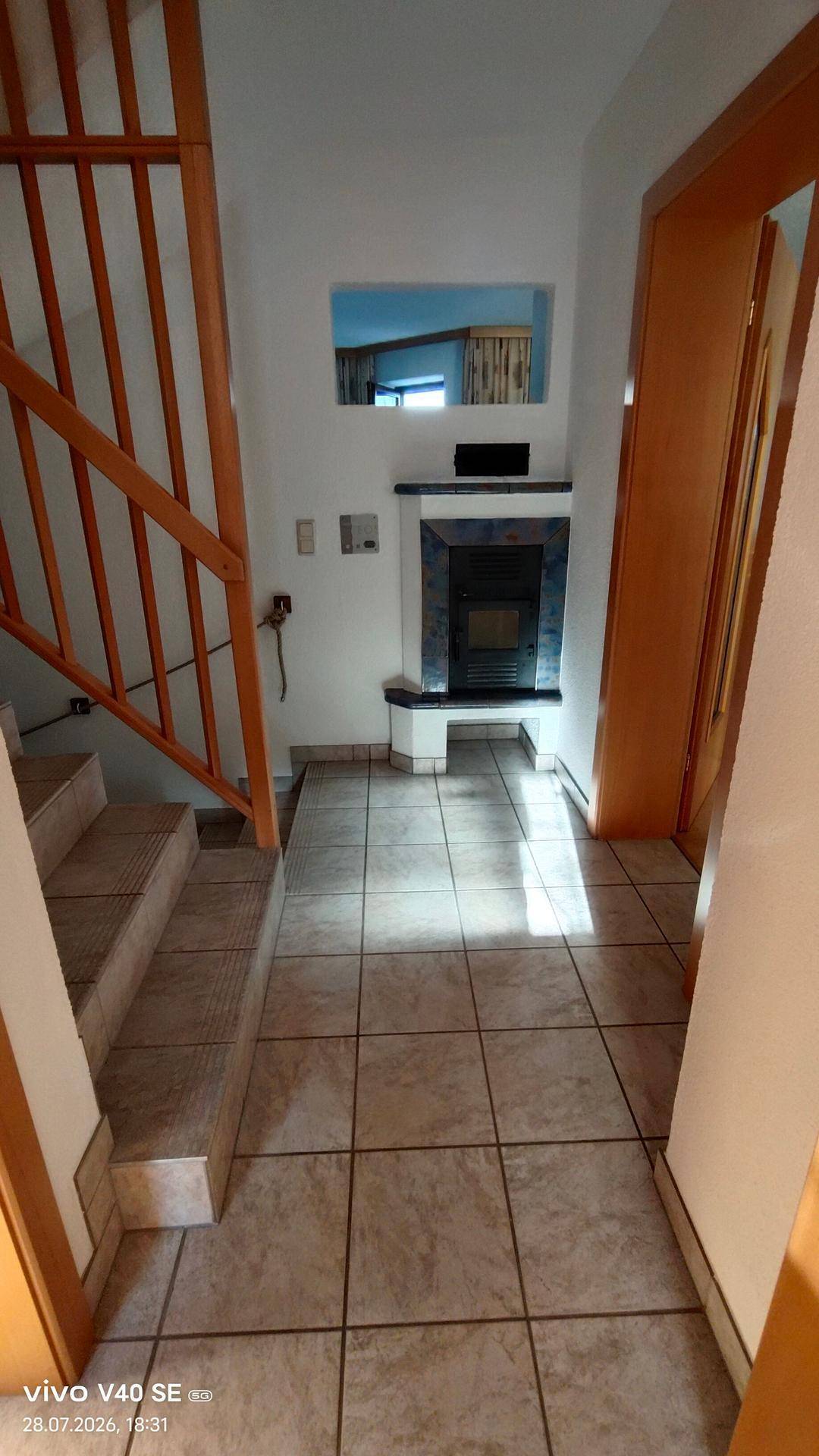 Heller Flur mit Fliesenboden, Holztreppe und einem integrierten Kamin für gemütliche Abende.