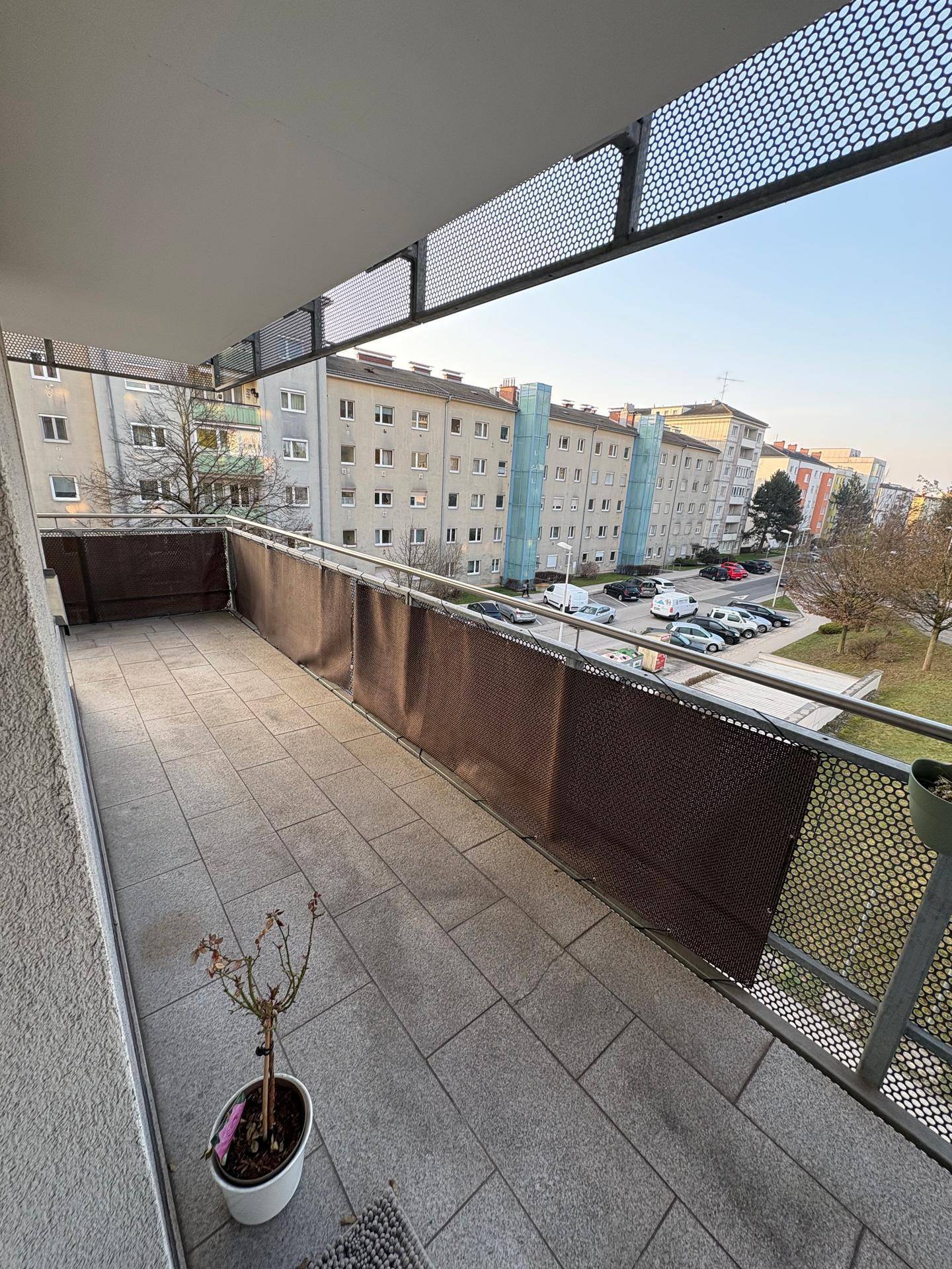 Langer Balkon mit Fliesenboden und Blick auf die umliegenden Wohngebäude und Parkplätze.
