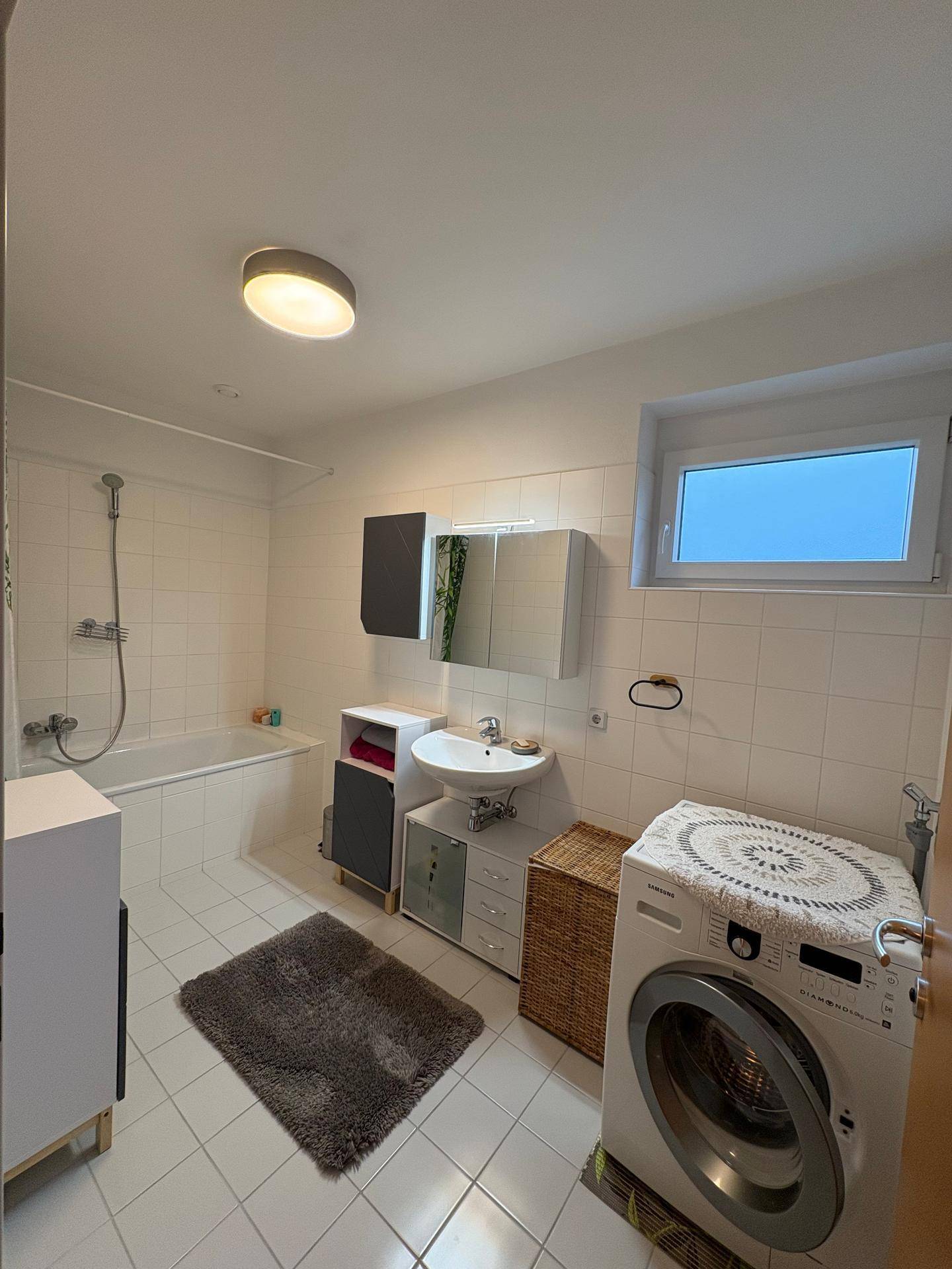 Gefliestes Badezimmer mit Badewanne, Waschbecken, Spiegelschrank und Waschmaschine.