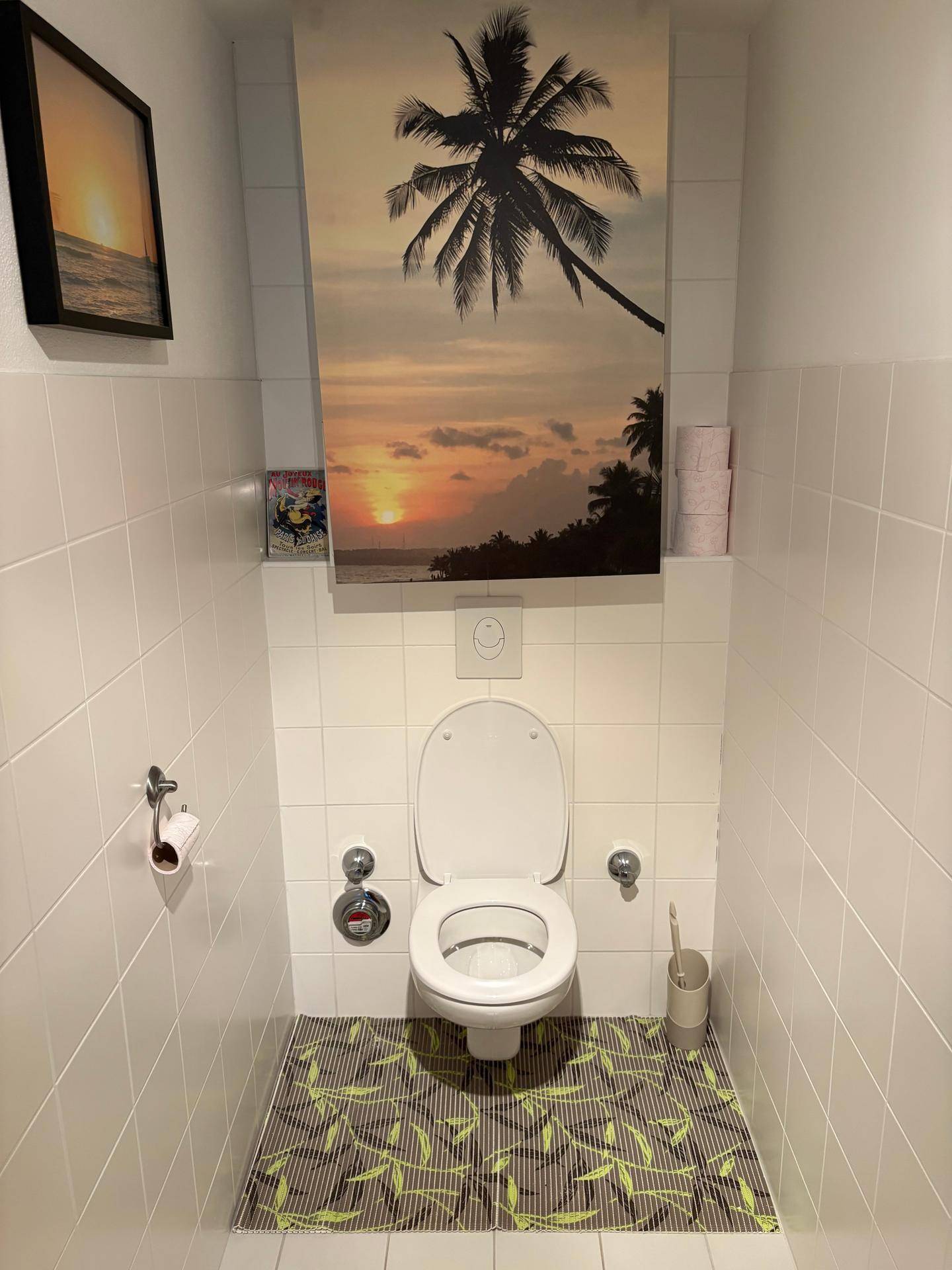 Separates WC mit Wand-WC und Fliesen an Wänden und Boden, dekoriert mit einem Bild.