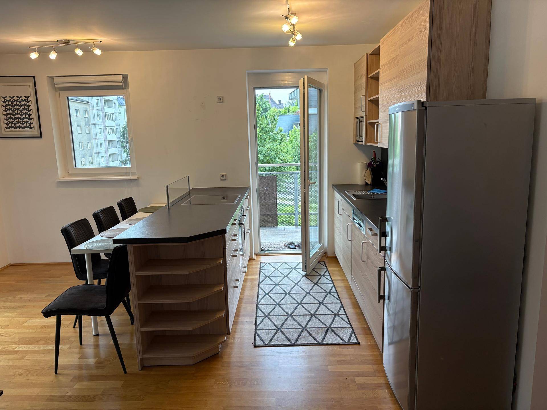 Funktionale Küche mit Holzschränken, dunkler Arbeitsplatte und direktem Balkonzugang.