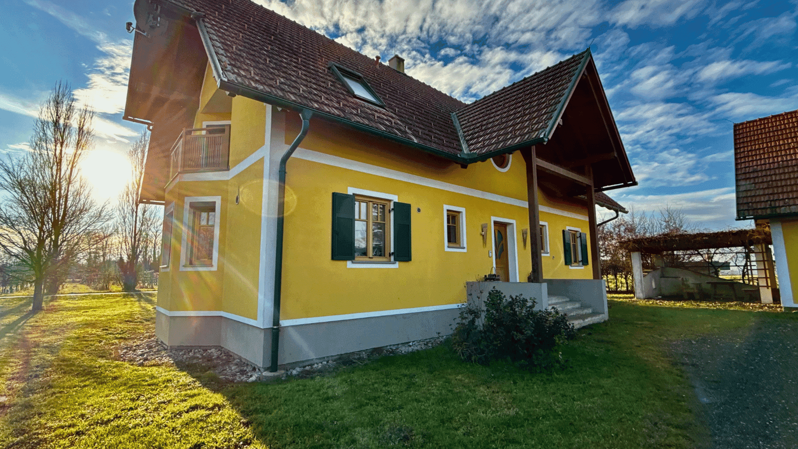 Sonniges gelbes Haus mit rotem Ziegeldach und einem kleinen Vorgarten. Die Fassade ist gut gepflegt.