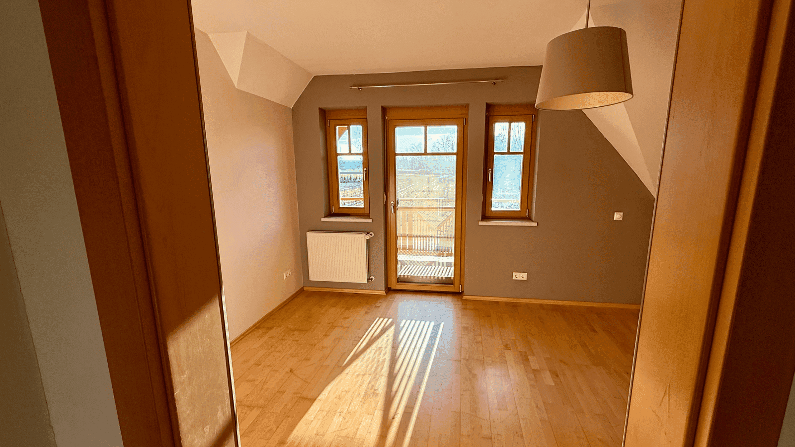 Helles Schlafzimmer mit Holzboden, Zugang zum Balkon und schrägen Decken.