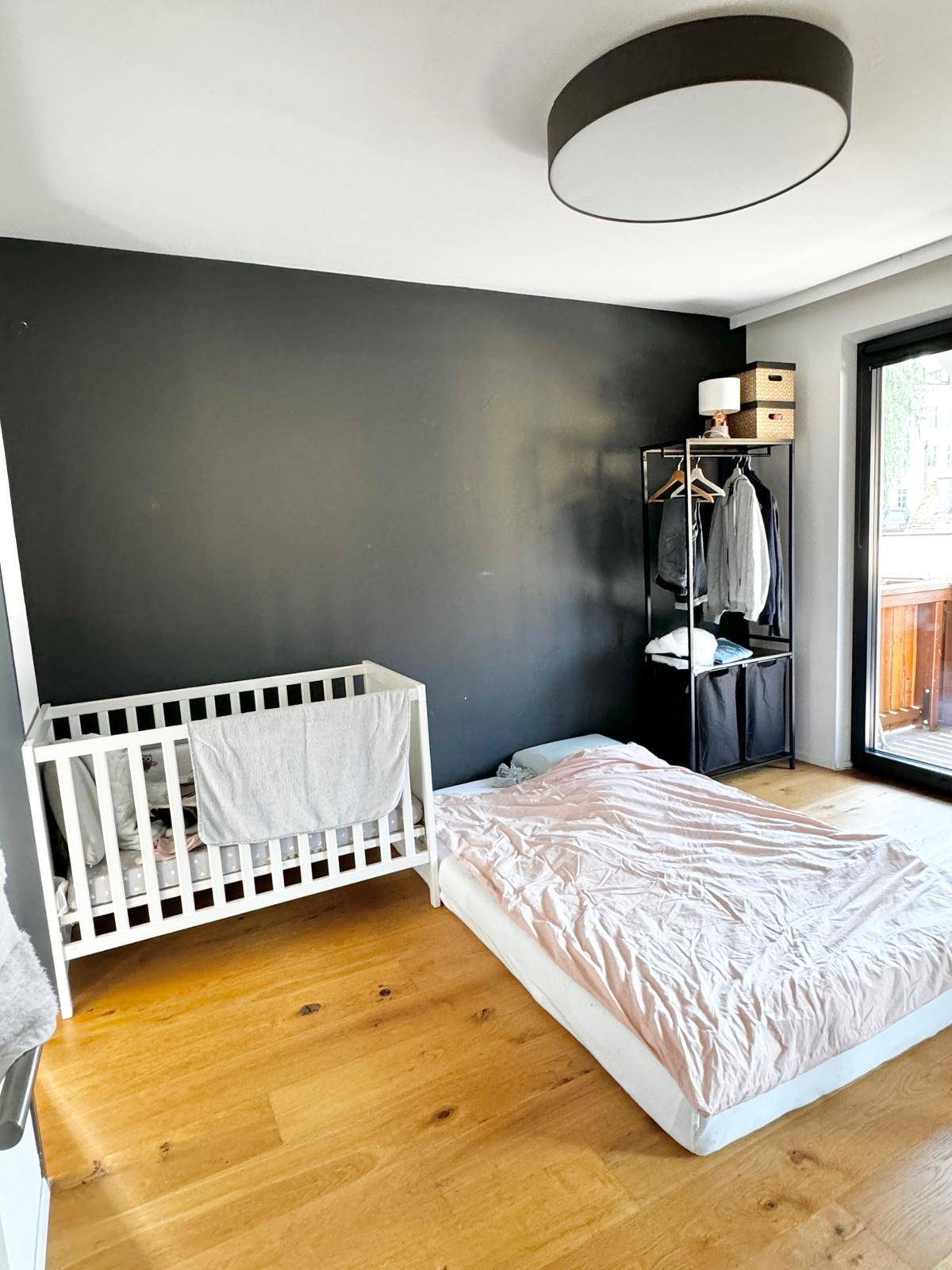 Schlafzimmer mit Babybett, einem Bett auf dem Boden und einem Kleiderständer.