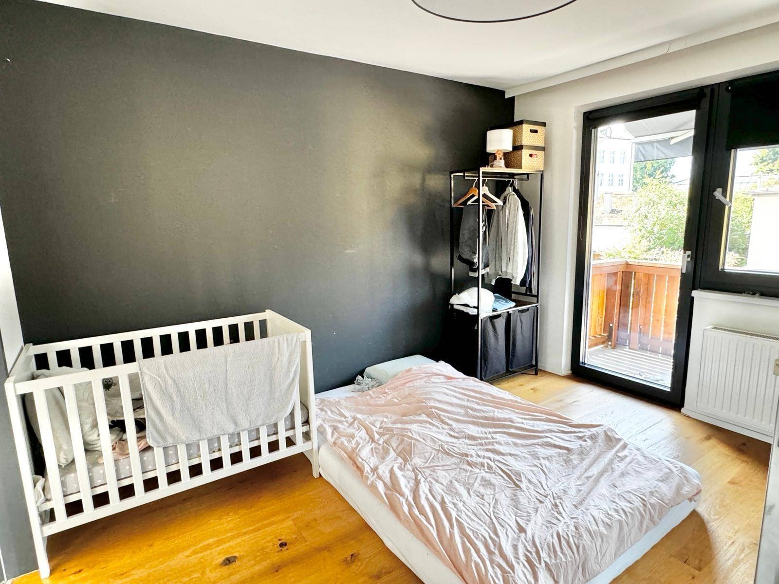 Gemütliches Schlafzimmer mit Babybett, einem Bett auf dem Boden und Zugang zum Balkon.