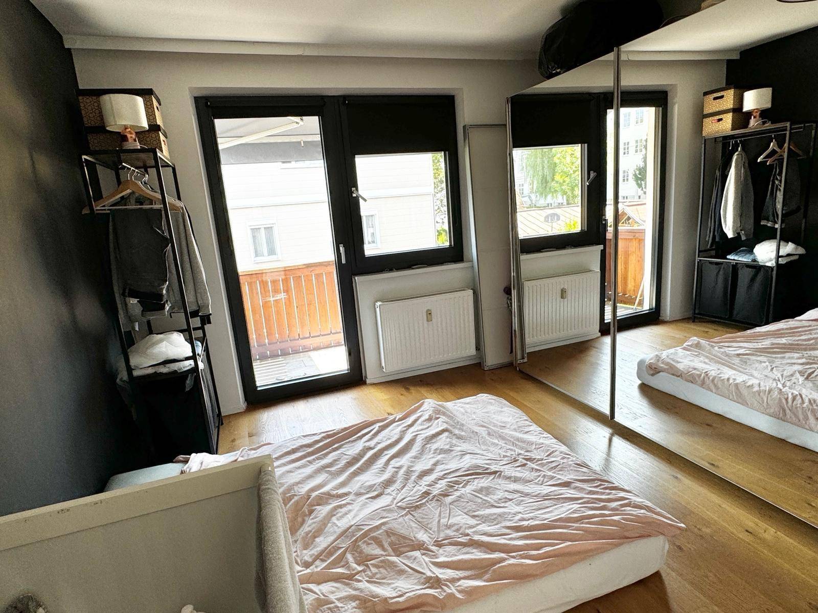 Schlafzimmer mit Holzboden, einem Bett, Babybett und zwei Türen, die auf einen Balkon führen.