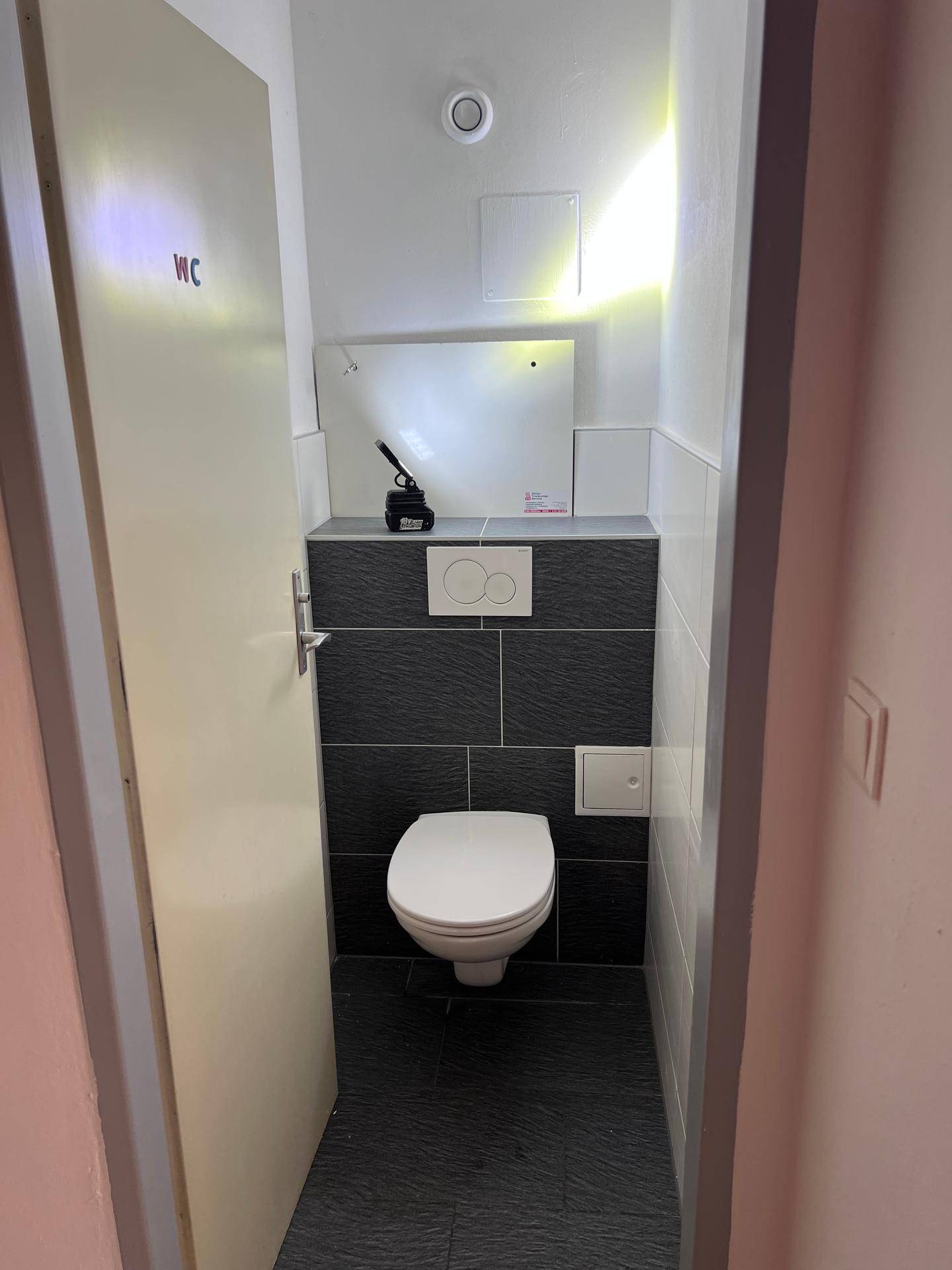 Separates WC mit wandhängender Toilette und modernen dunklen Fliesen, sauber und funktional gestaltet.