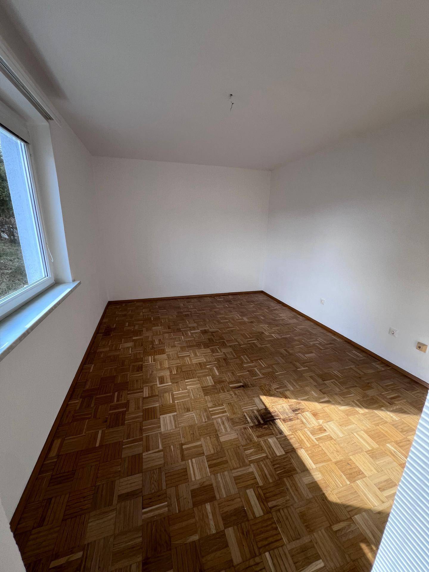 Ruhiges Schlafzimmer mit Parkettboden und einem Fenster, das viel Tageslicht hereinlässt und eine grüne Aussicht bietet.