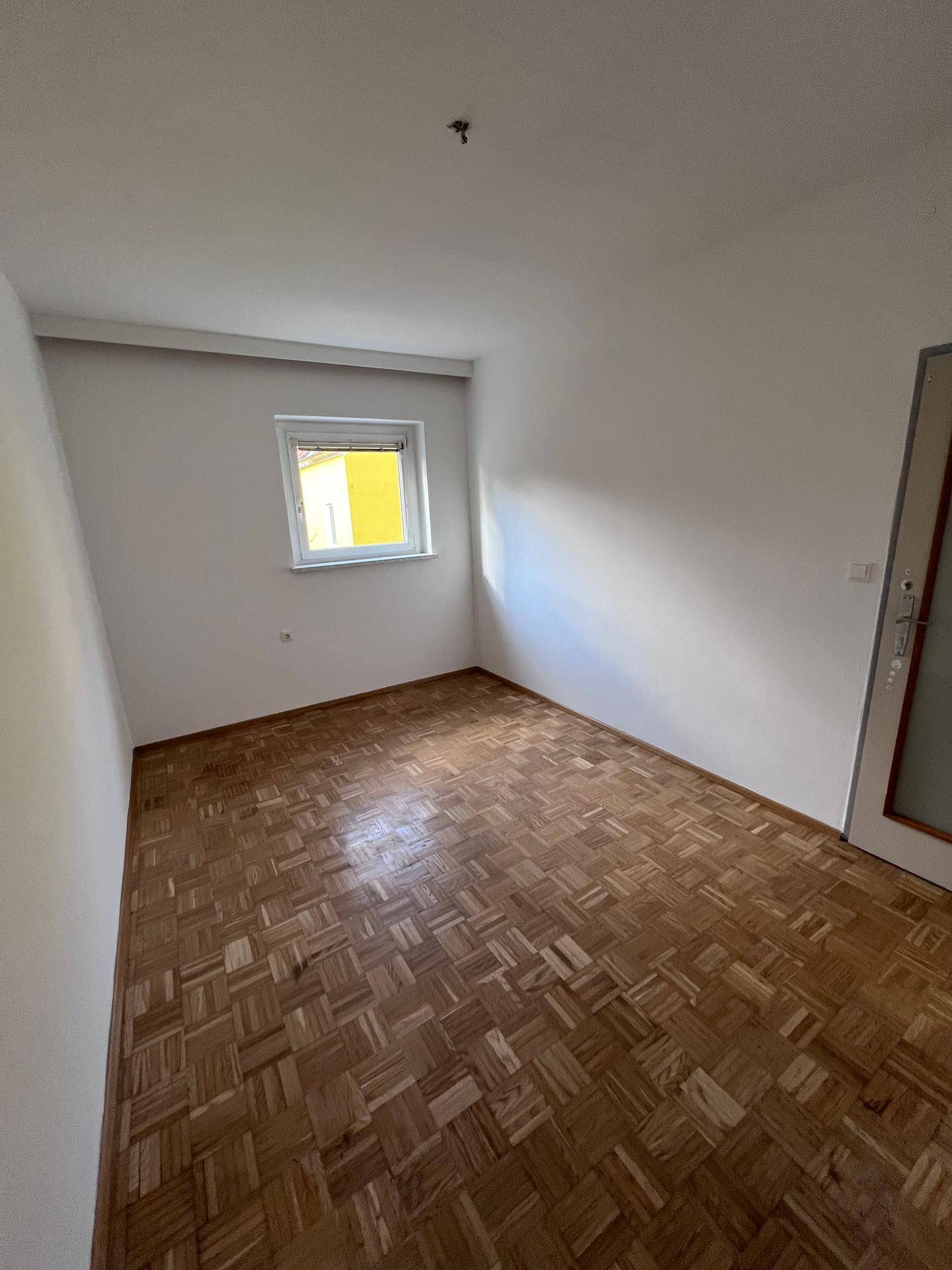 Gemütliches Schlafzimmer mit Parkettboden und einem Fenster, das viel Sonnenlicht einfängt und hell ist.