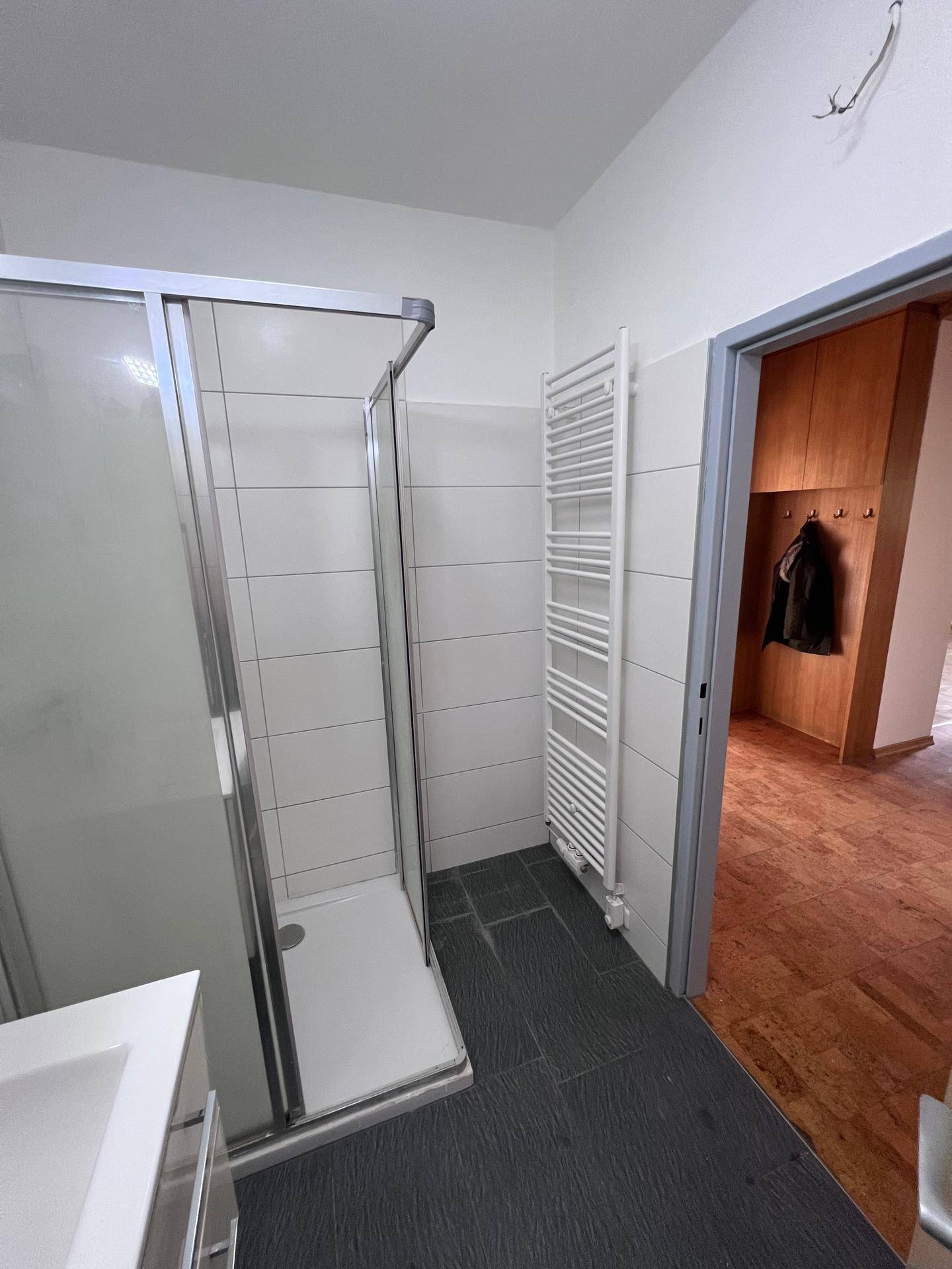 Badezimmer mit Duschkabine und beheiztem Handtuchhalter, angrenzend an einen Flur, praktisch und komfortabel.