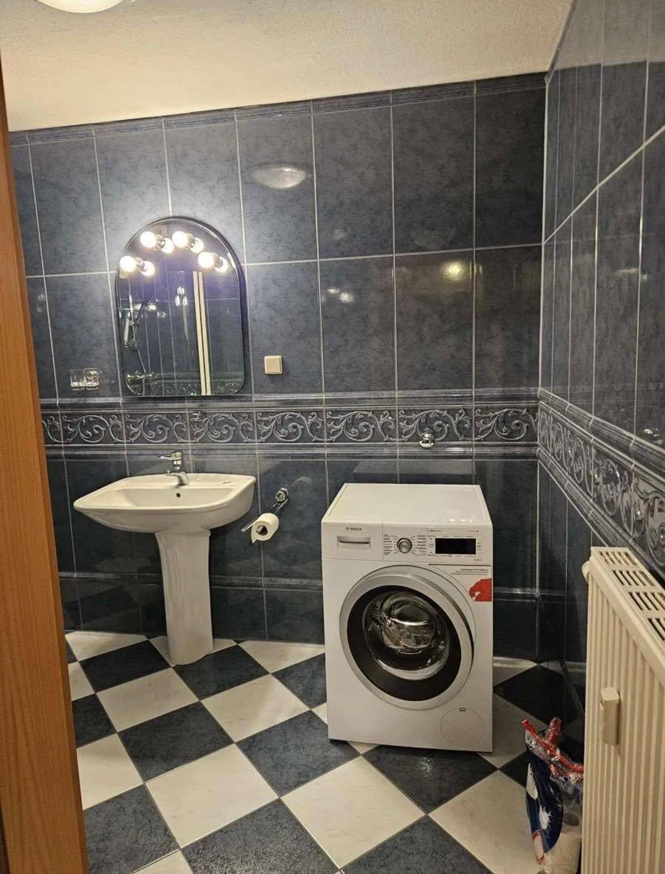 Badezimmer mit blau-weiß karierten Fliesen, Waschbecken und Waschmaschine.