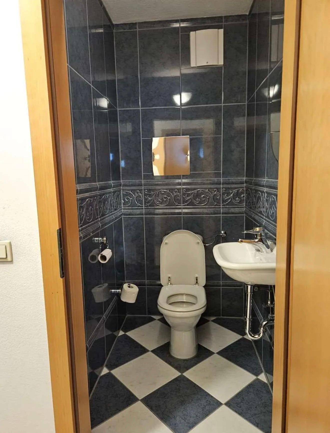 Kleines Gäste-WC mit blau-weiß karierten Fliesen, Toilette und Handwaschbecken.