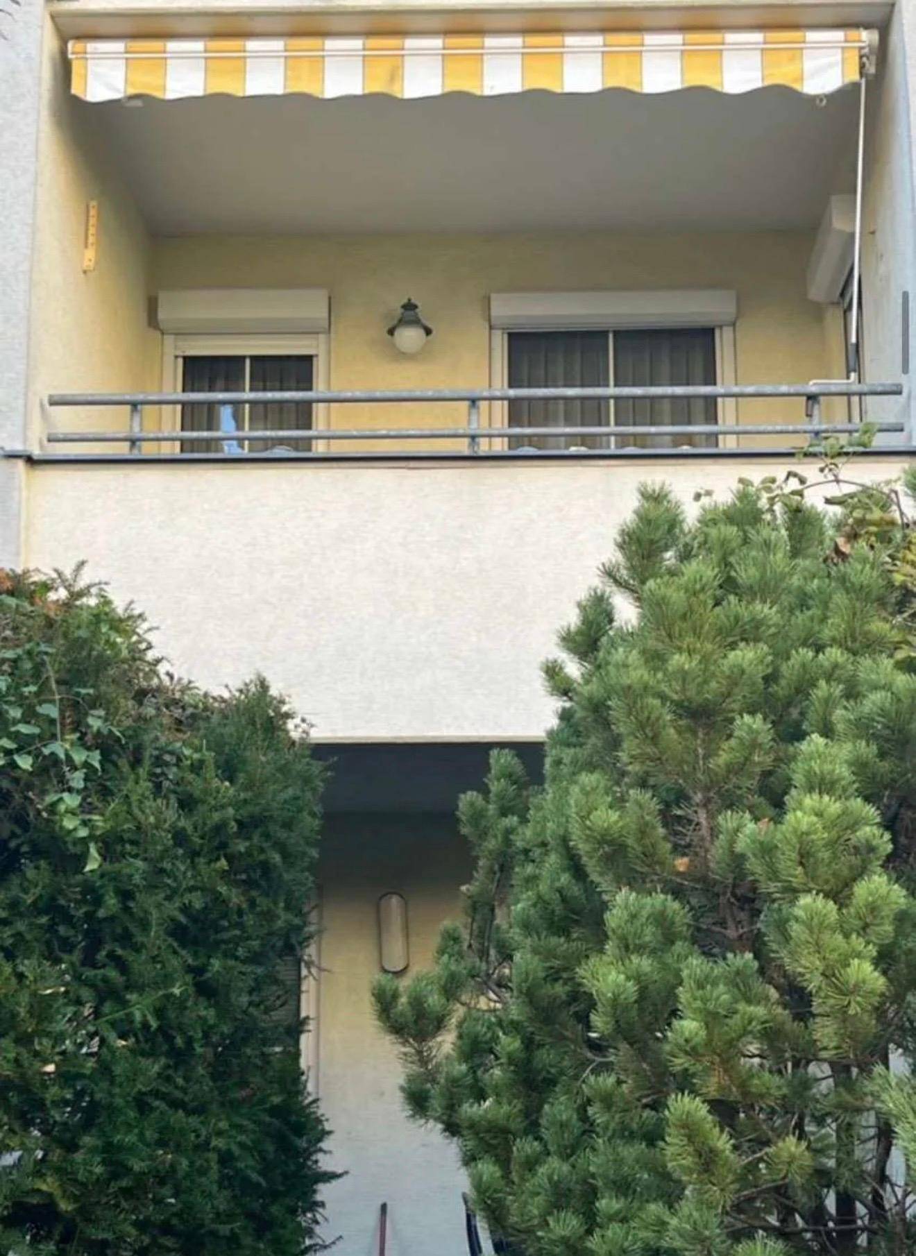 Balkon mit gelb-weiß gestreifter Markise und Blick auf grüne Büsche.