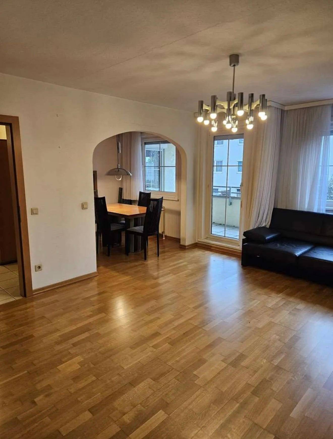 Offener Wohn-Essbereich mit Parkettboden, Esstisch und Zugang zum Balkon.