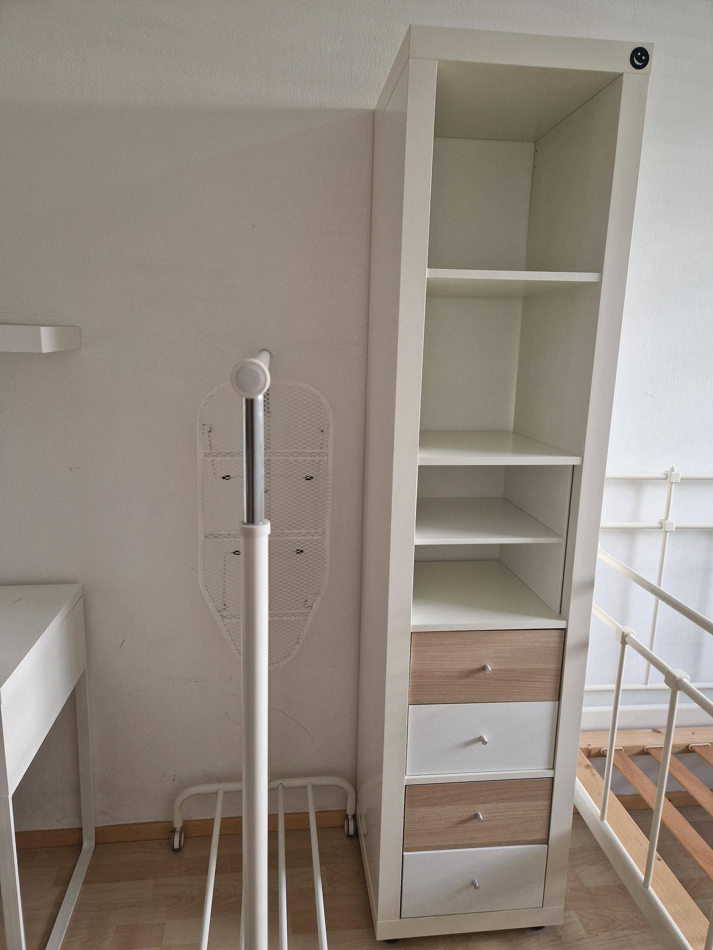 Schlafzimmer mit hohem Regal, Kleiderständer und weißem Metallbettgestell.