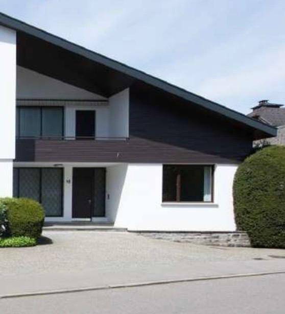 Ansicht des modernen Hauses mit weißer Fassade, dunklem Dach und gepflegter Hecke.