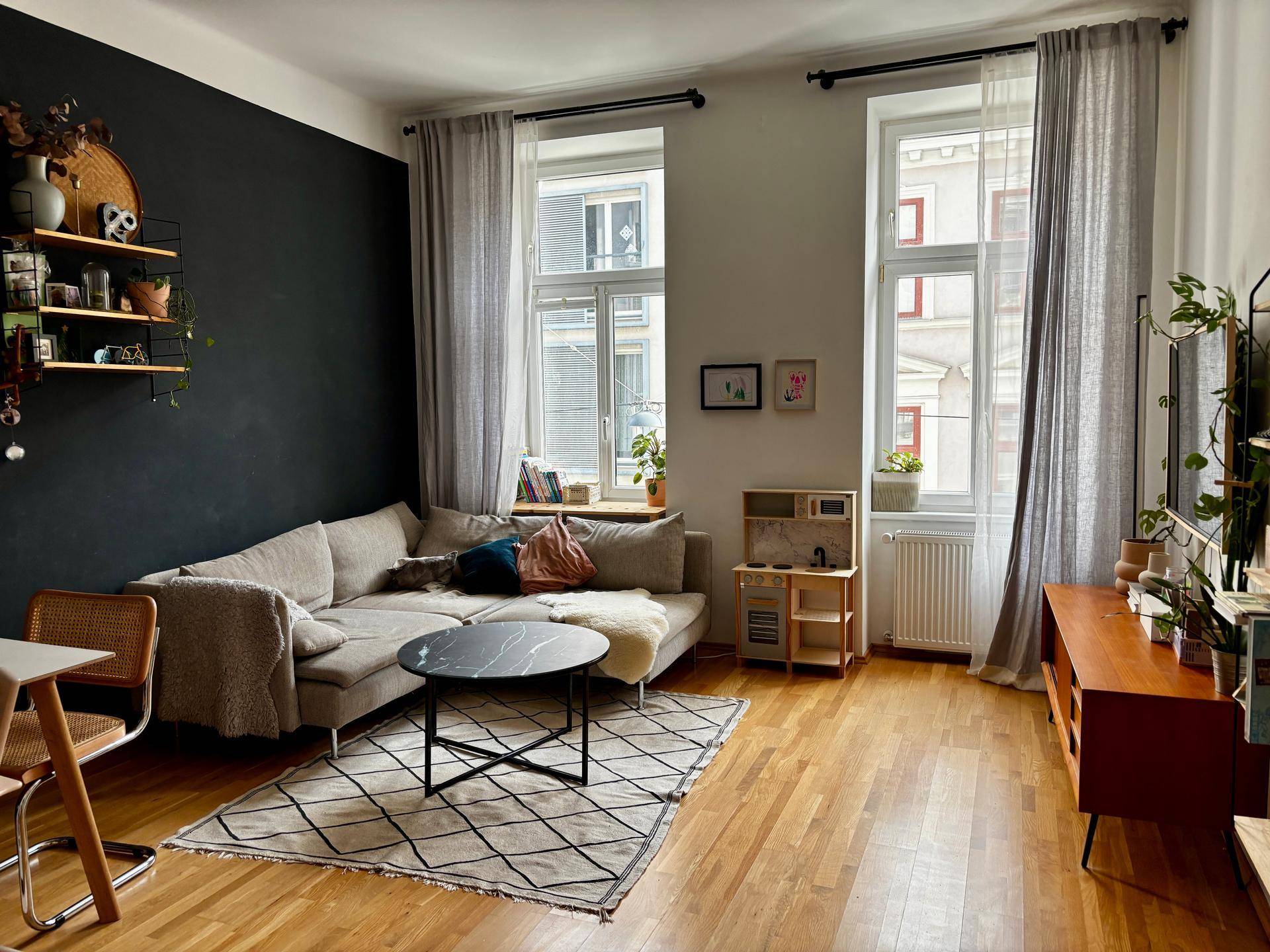 Modernes Wohnzimmer mit Ecksofa, Holzboden und dunkler Akzentwand.