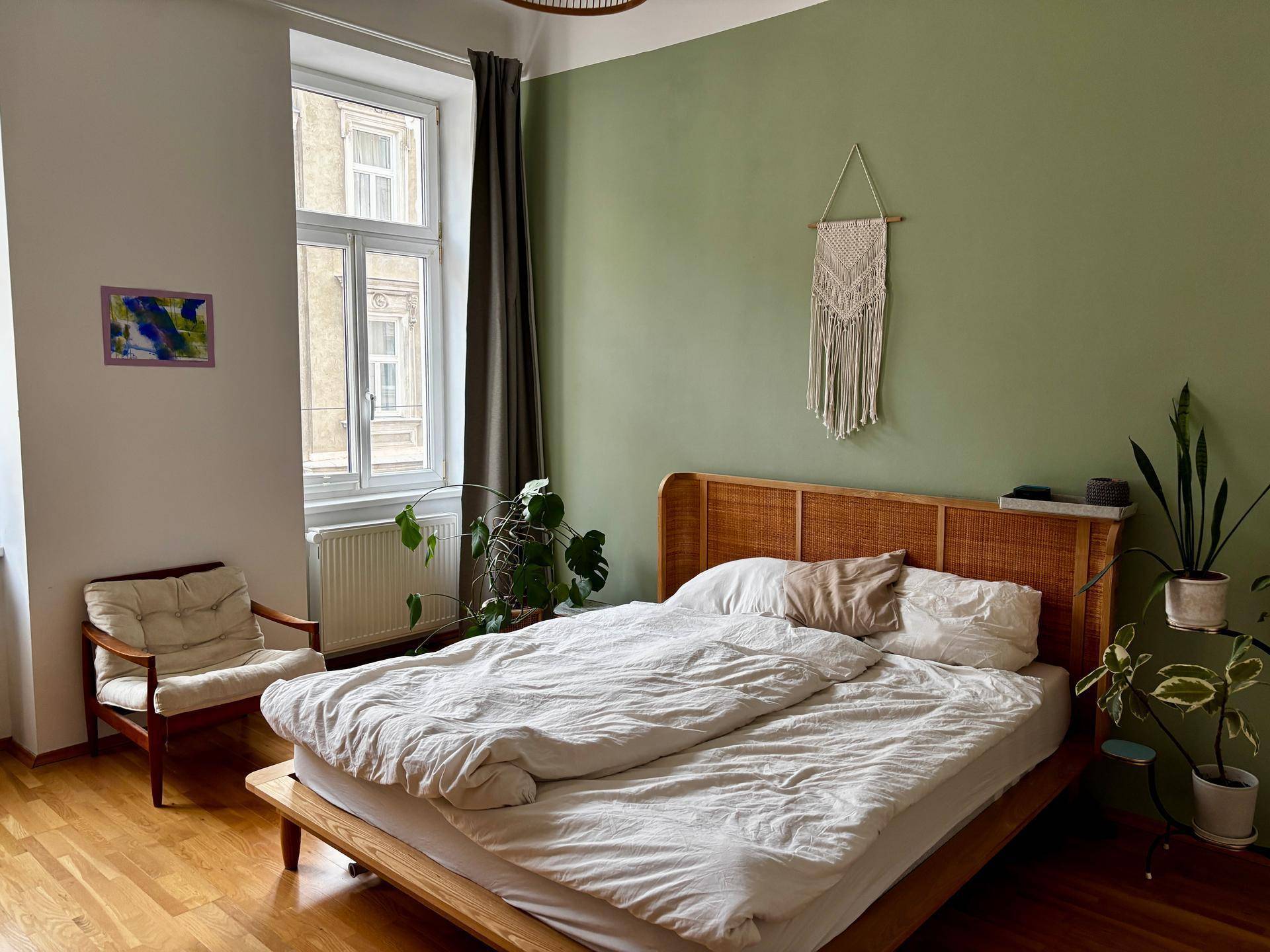 Gemütliches Schlafzimmer mit Holzbett, grüner Wand und Blick auf die Straße.