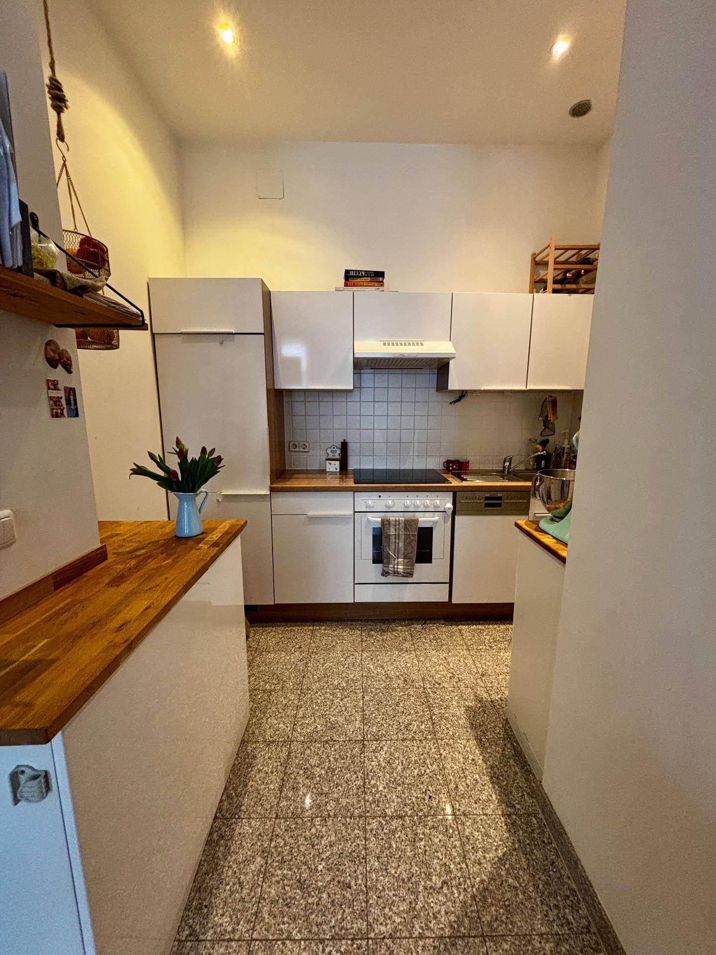 Funktionale Küche mit weißen Schränken, Holzarbeitsplatten und Fliesenboden.