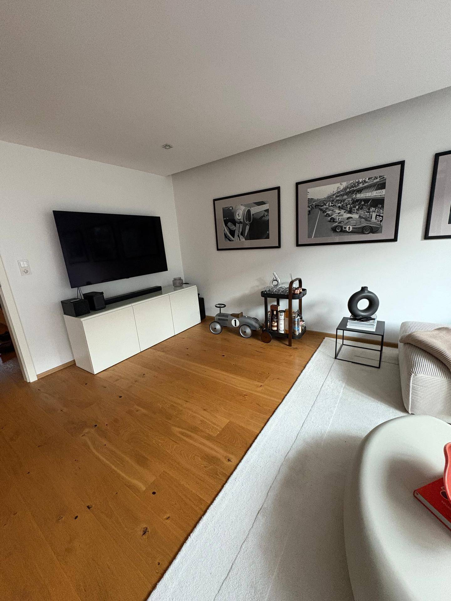 Moderner Wohnbereich mit großem Fernseher, Sideboard und Holzboden.