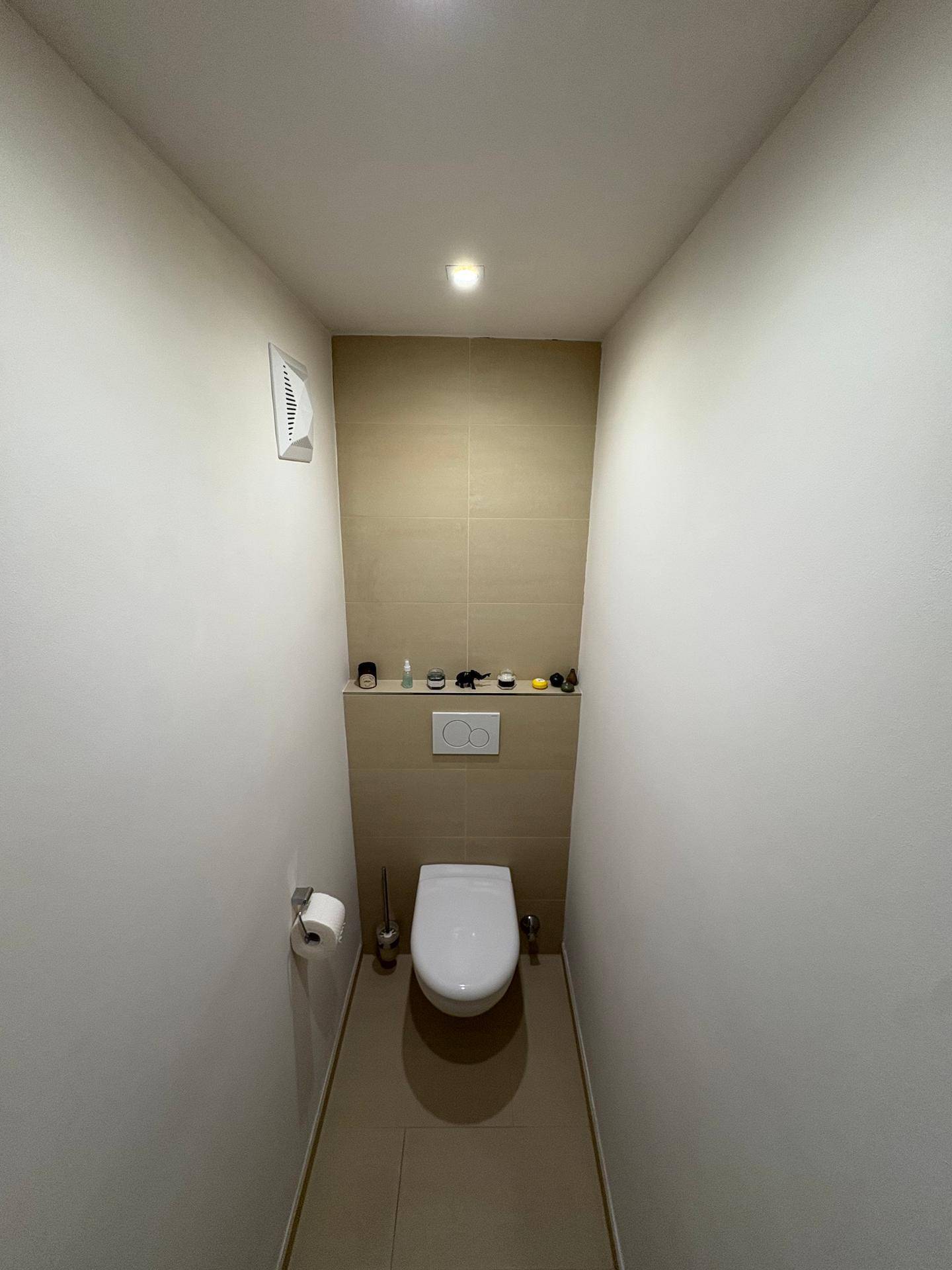 Separates WC mit Wand-WC und beigen Fliesen an der Wand.
