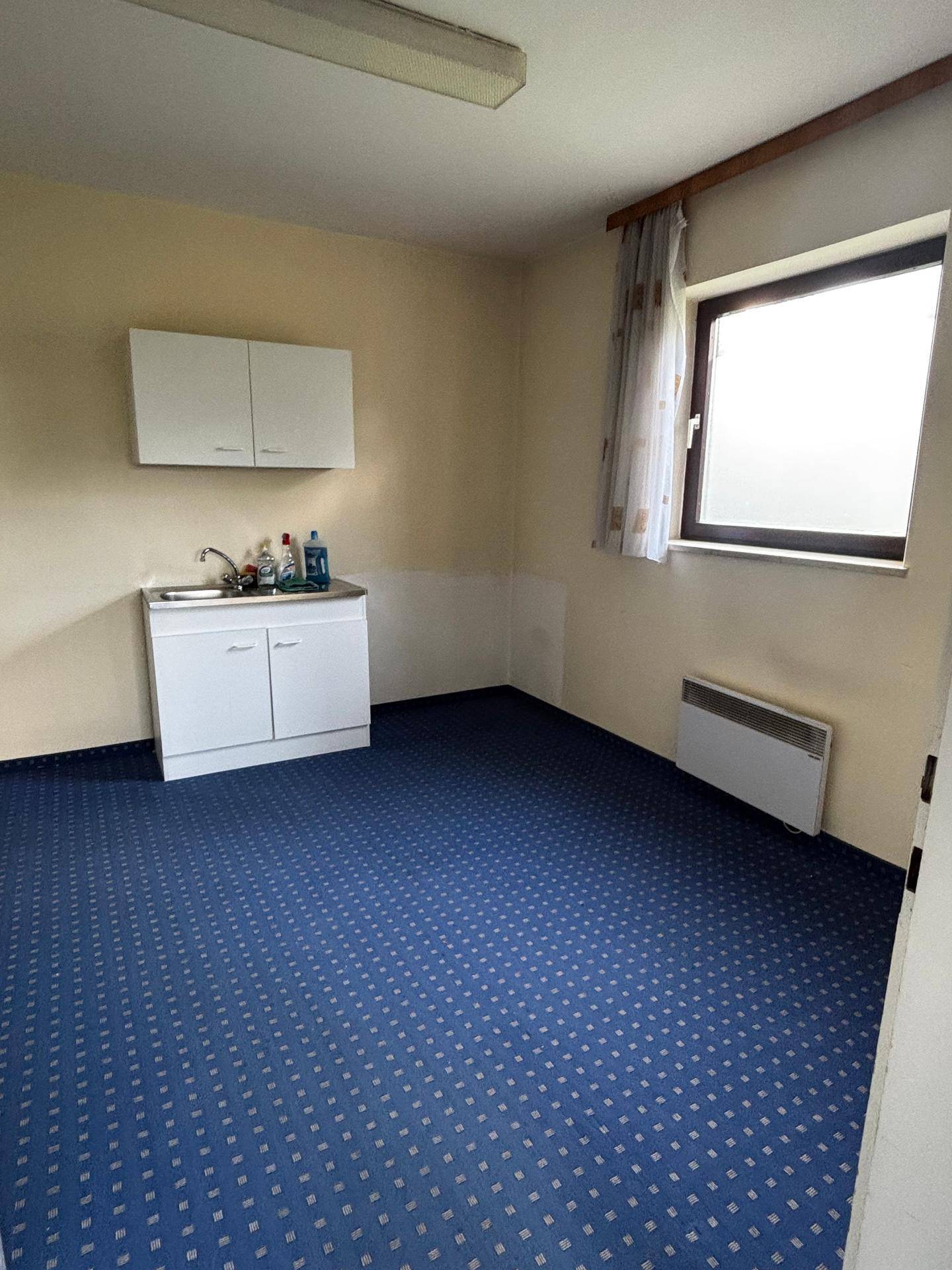 Kleine Küchenzeile mit Spülbecken, Unterschränken und einem Fenster, ideal für Pausen.