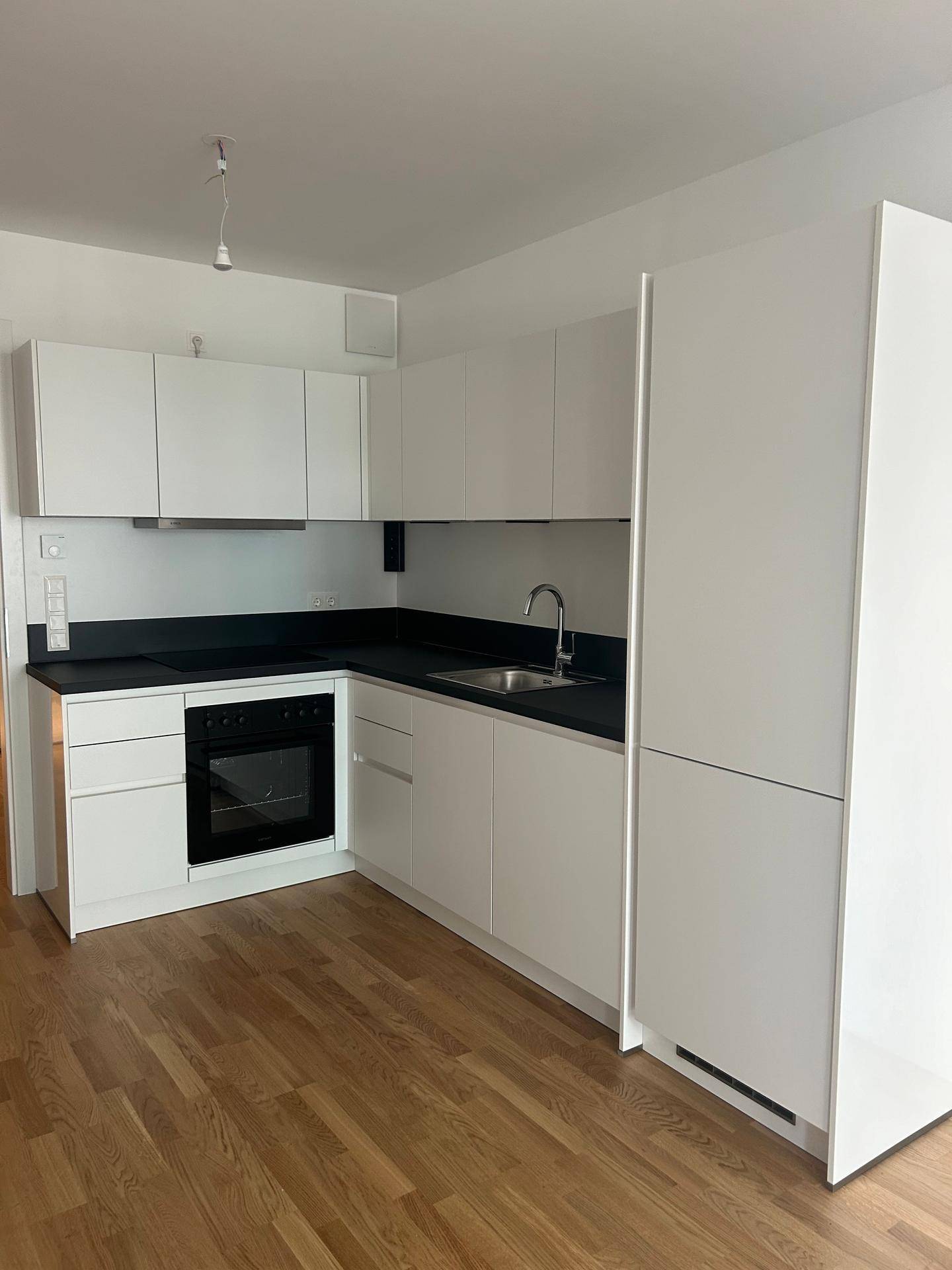 Moderne Einbauküche in Weiß mit dunkler Arbeitsplatte und integrierten Geräten, funktional und stilvoll.