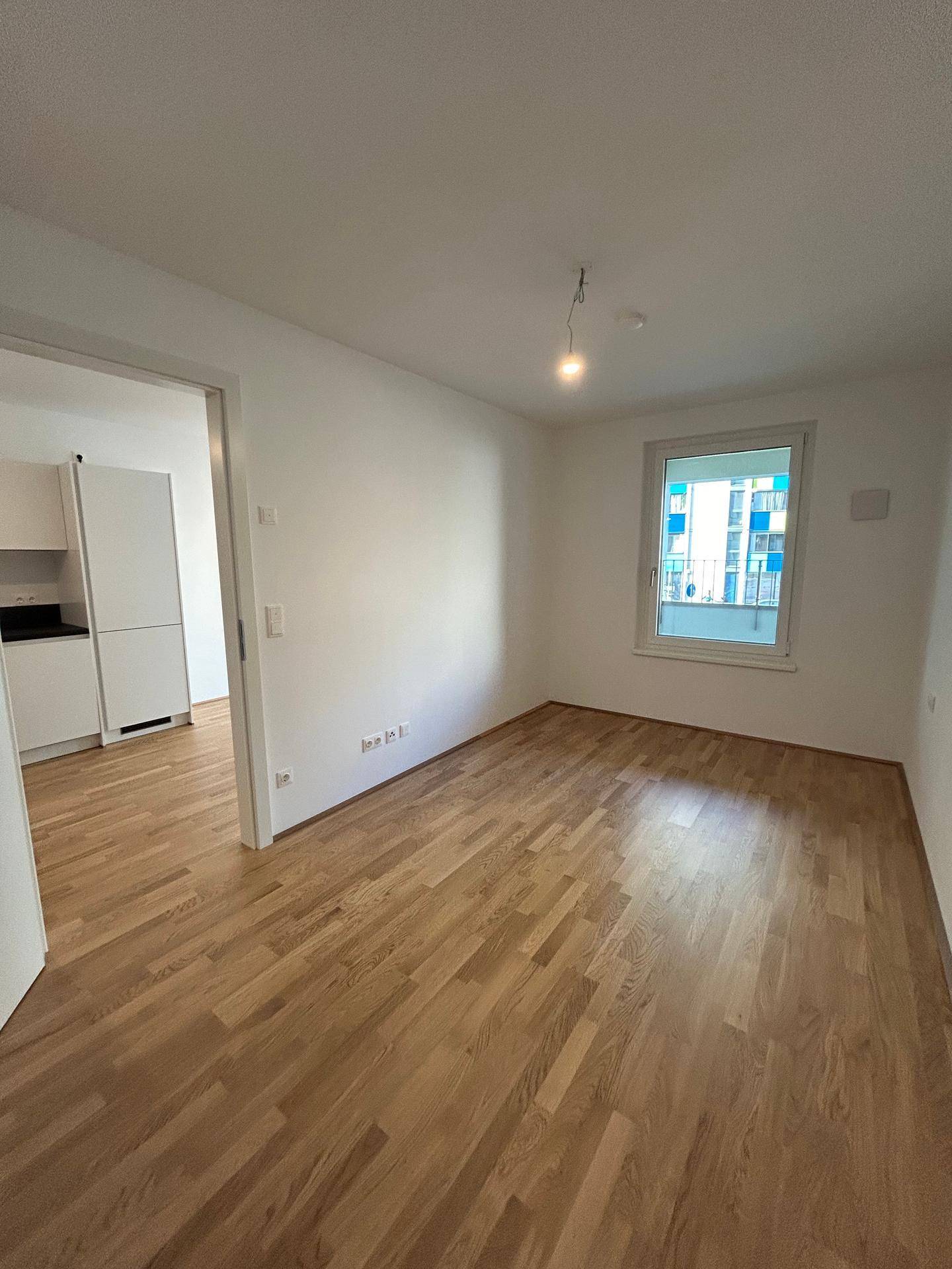 Heller Wohnbereich mit Eichenparkett und großem Fenster, bietet viel Tageslicht und eine angenehme Atmosphäre.
