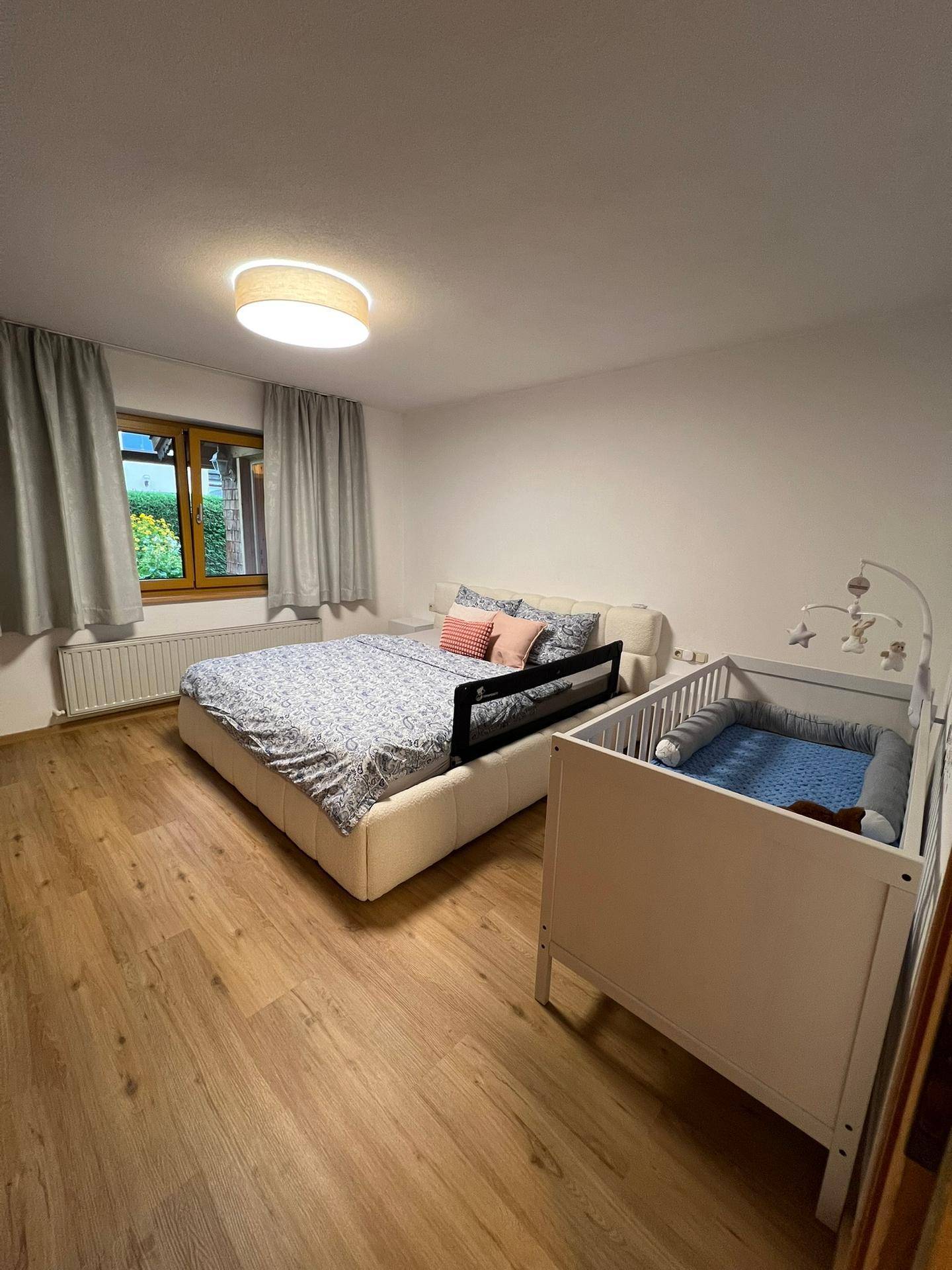 Schlafzimmer mit Doppelbett, Babybett und Blick ins Grüne durch das Fenster.