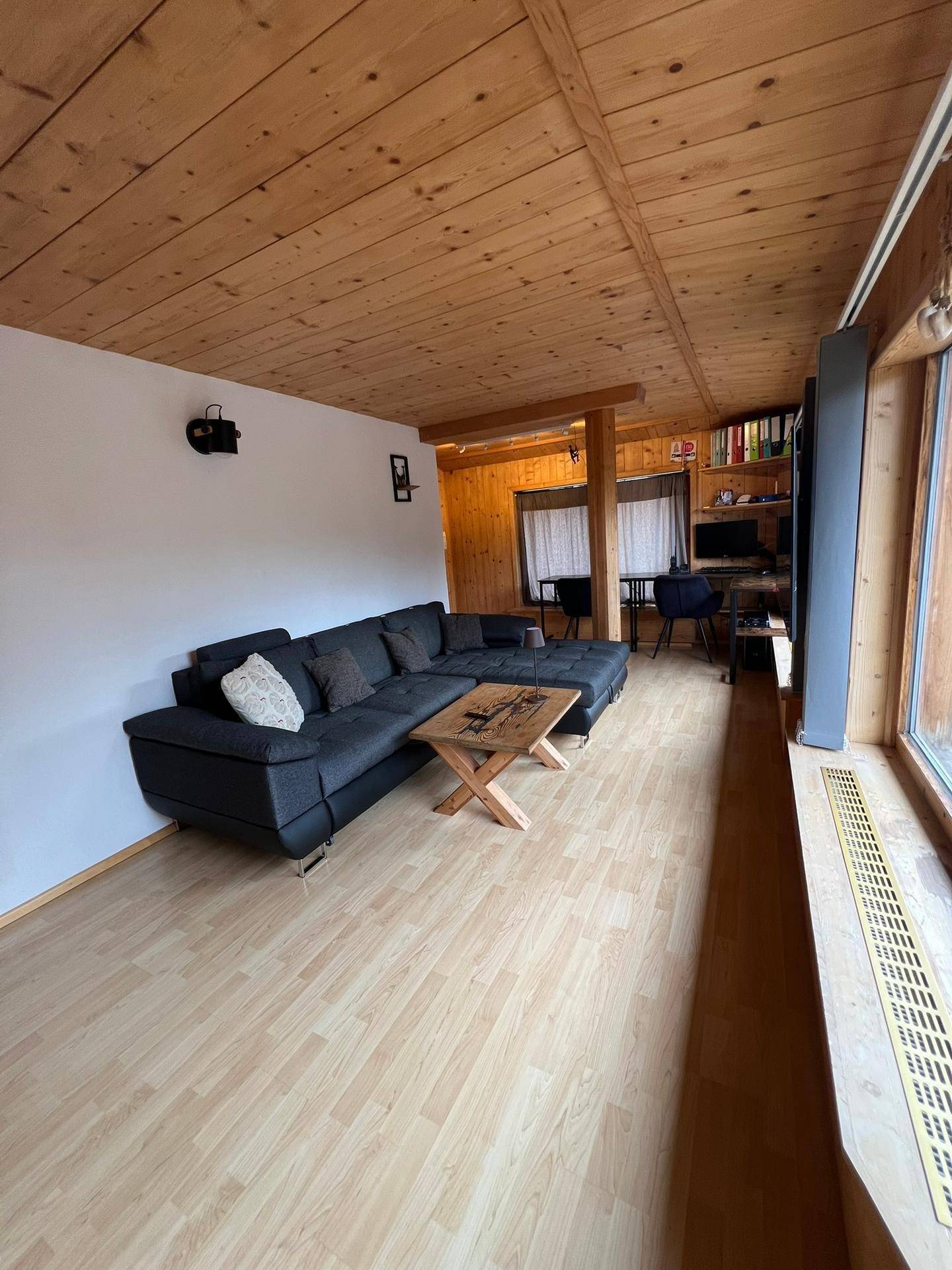 Gemütliches Wohnzimmer mit großem Sofa, Holzdecke und weitem Blick durch die Fenster.