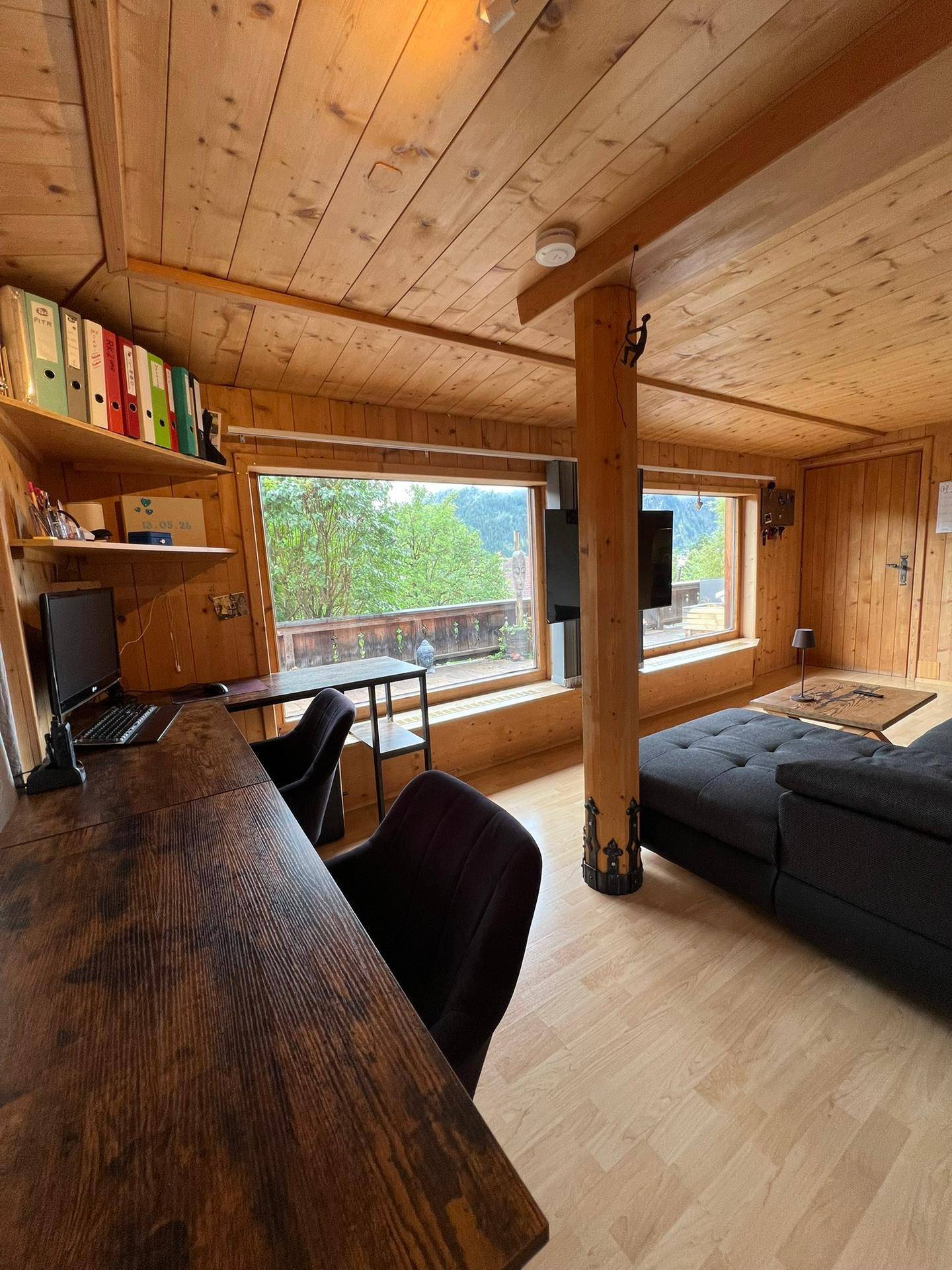 Wohn- und Arbeitsbereich mit Schreibtisch, Sofa, Holzdecke und weitem Blick ins Grüne.