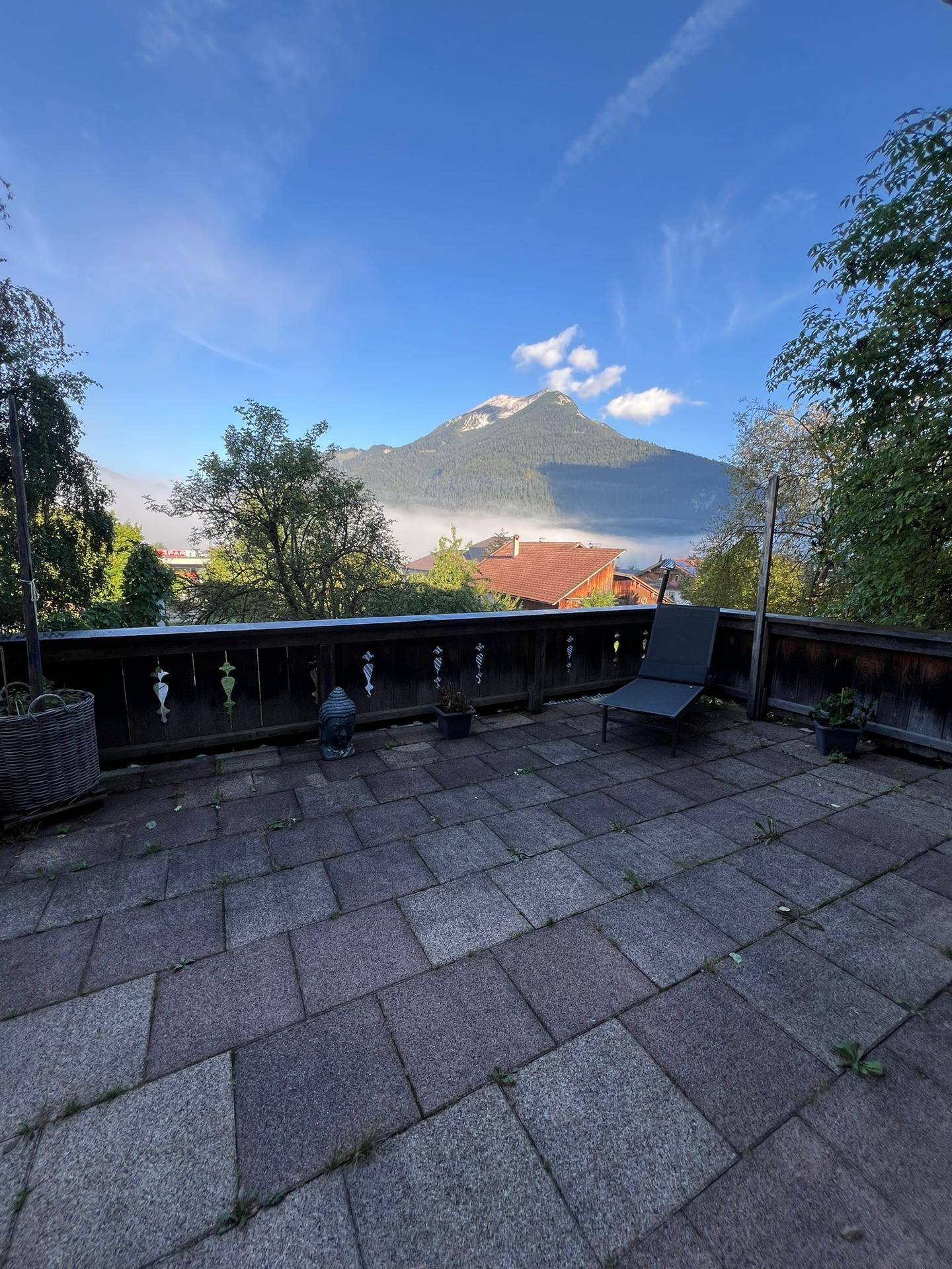 Große gepflasterte Terrasse mit Liegestuhl und atemberaubendem Bergblick unter blauem Himmel.