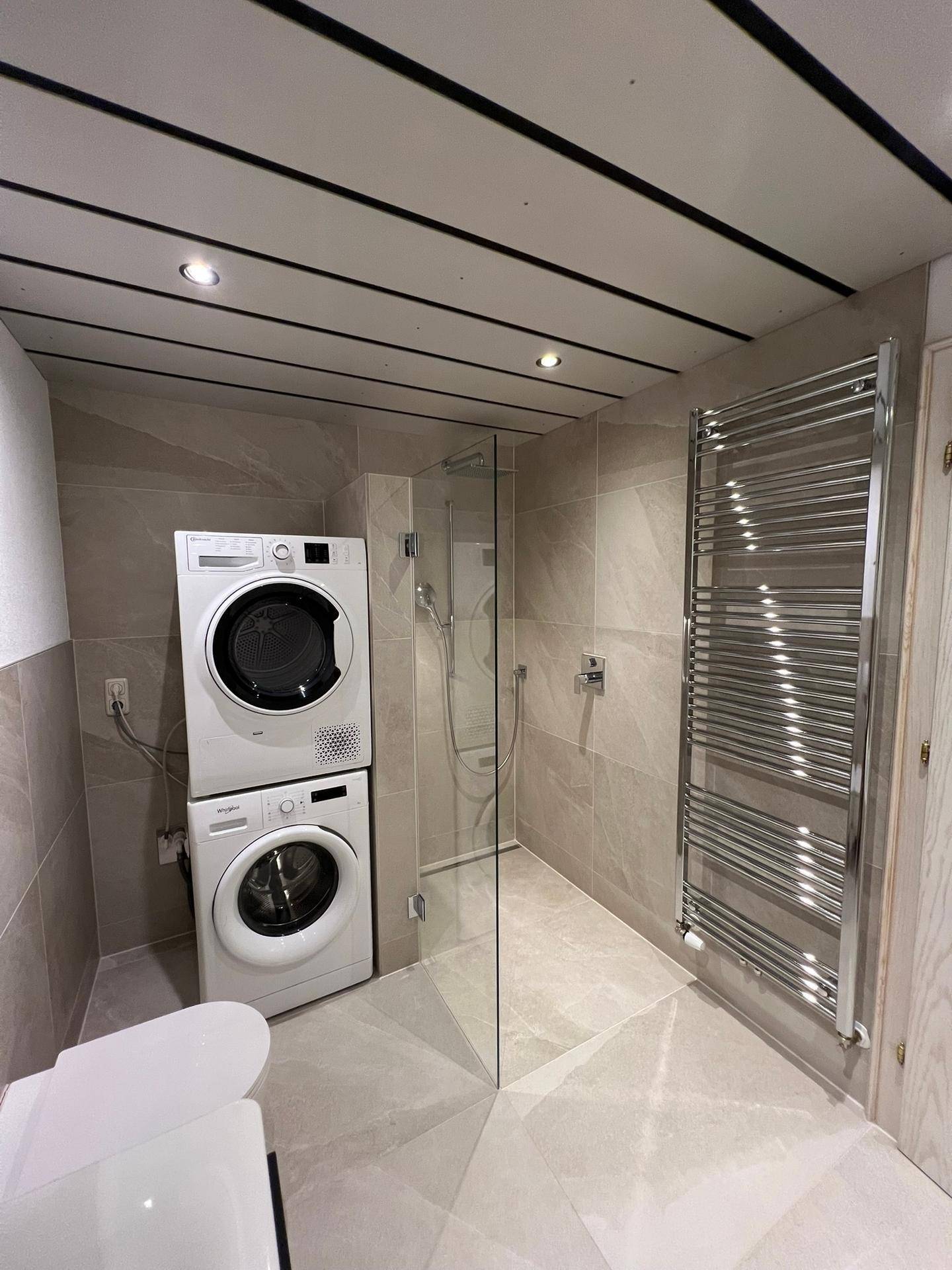 Helles Badezimmer mit Dusche, Waschmaschine, Trockner und beheiztem Handtuchhalter.