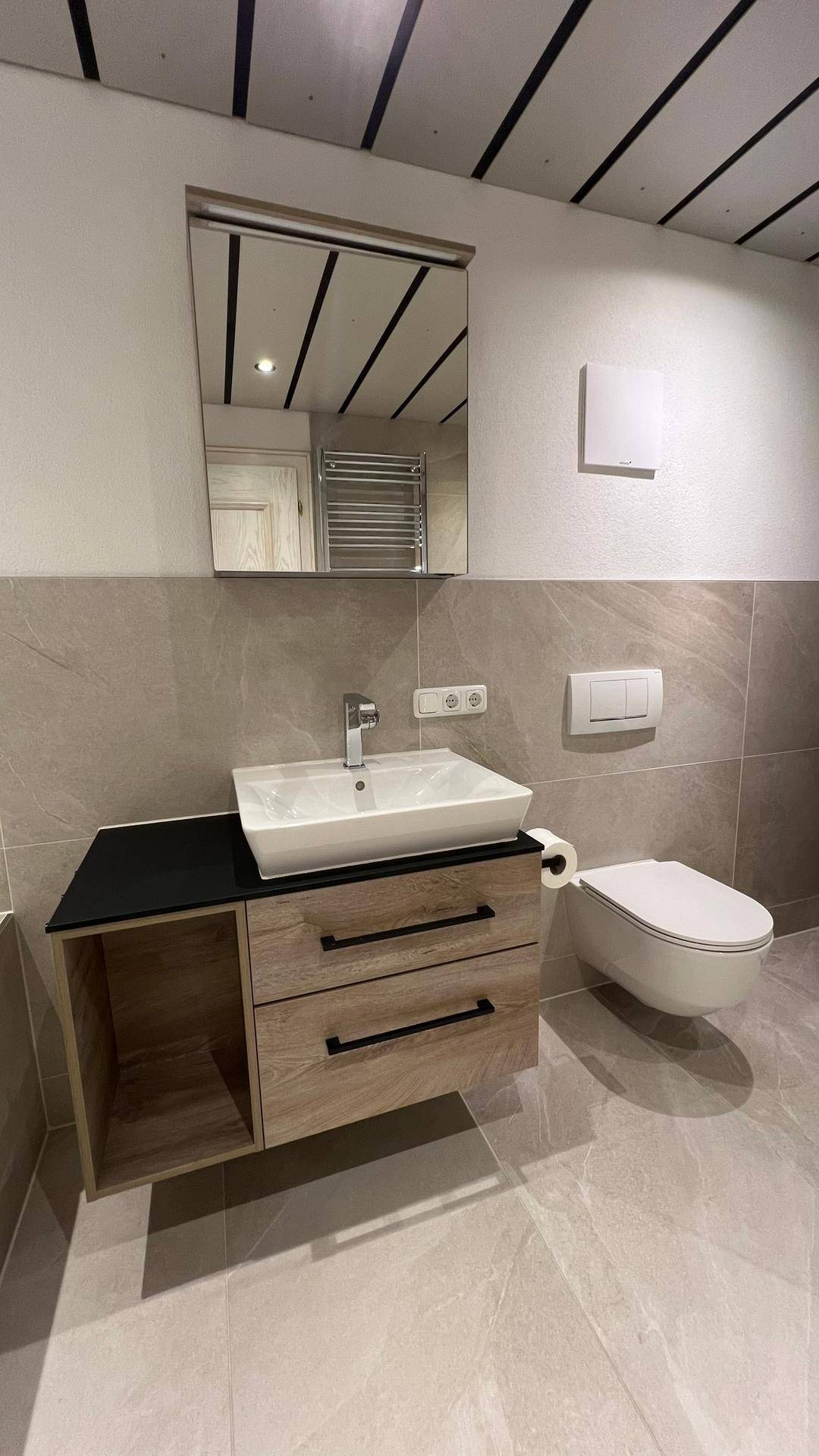 Modernes Badezimmer mit Waschbecken, Spiegel, wandhängendem WC und hellen Fliesen.
