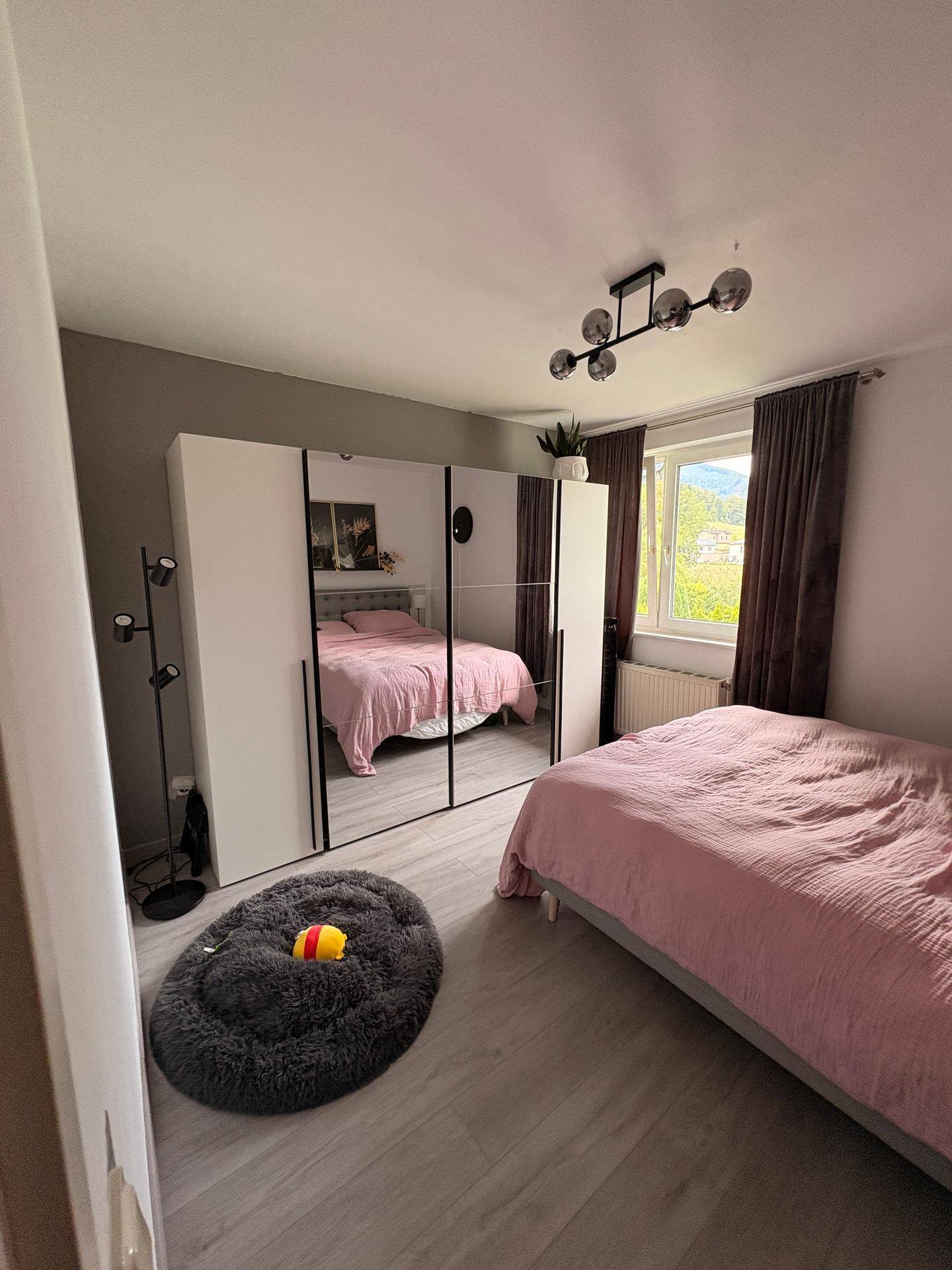 Helles Schlafzimmer mit Doppelbett, großem Spiegelschrank und Blick ins Grüne.