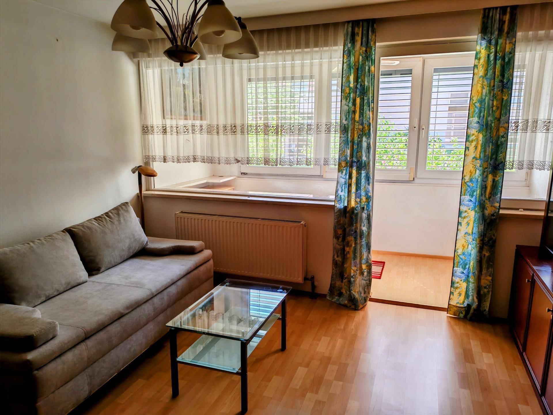 Helles Wohnzimmer mit beigem Sofa, Glascouchtisch und Blick ins Grüne vom Balkon.